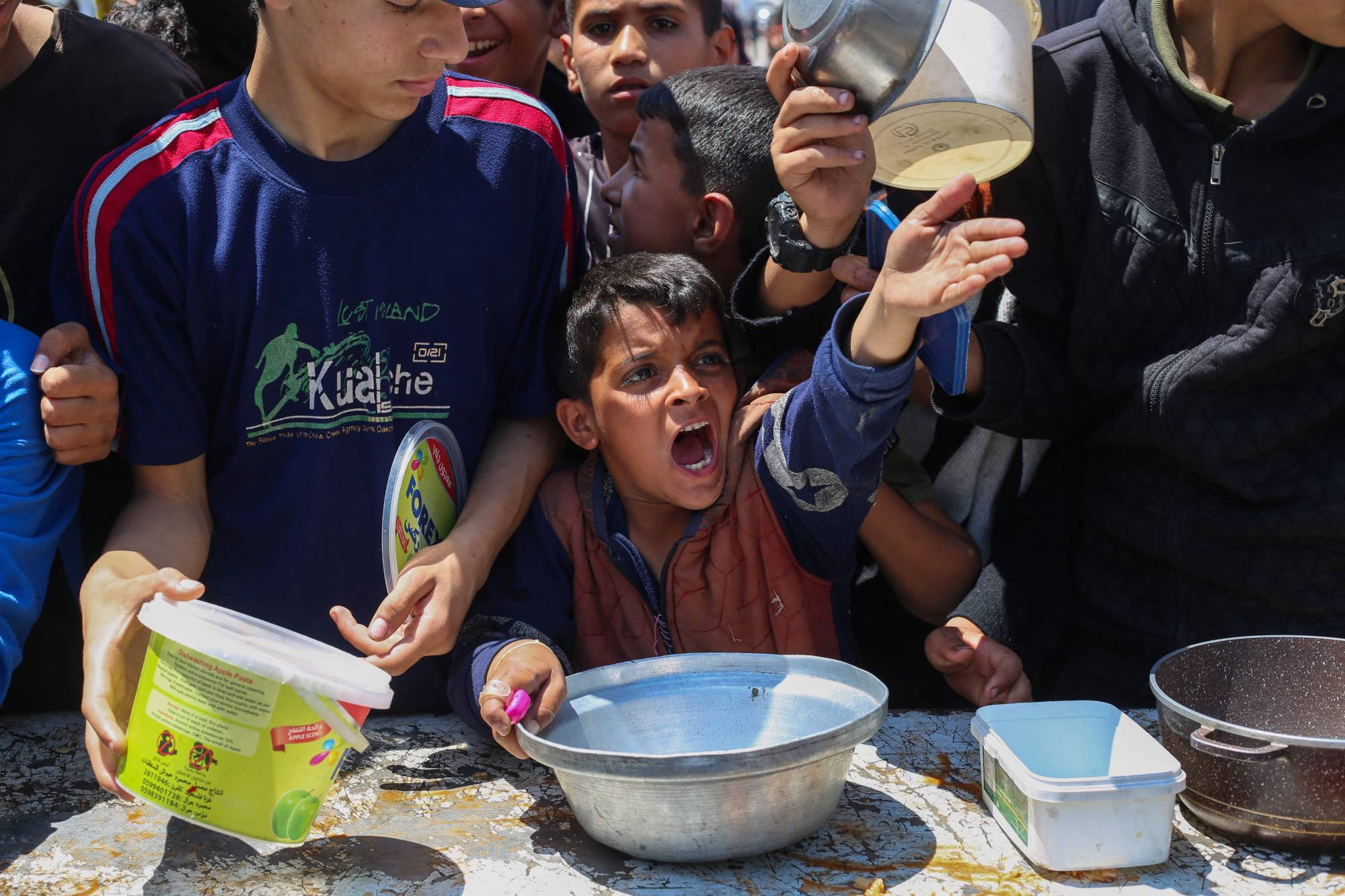 صبي فلسطيني مع أقرانه في أثناء الحصول على الطعام من مطبخ خيري في مخيم النصيرات وسط غزة أمس (أ.ف.ب)