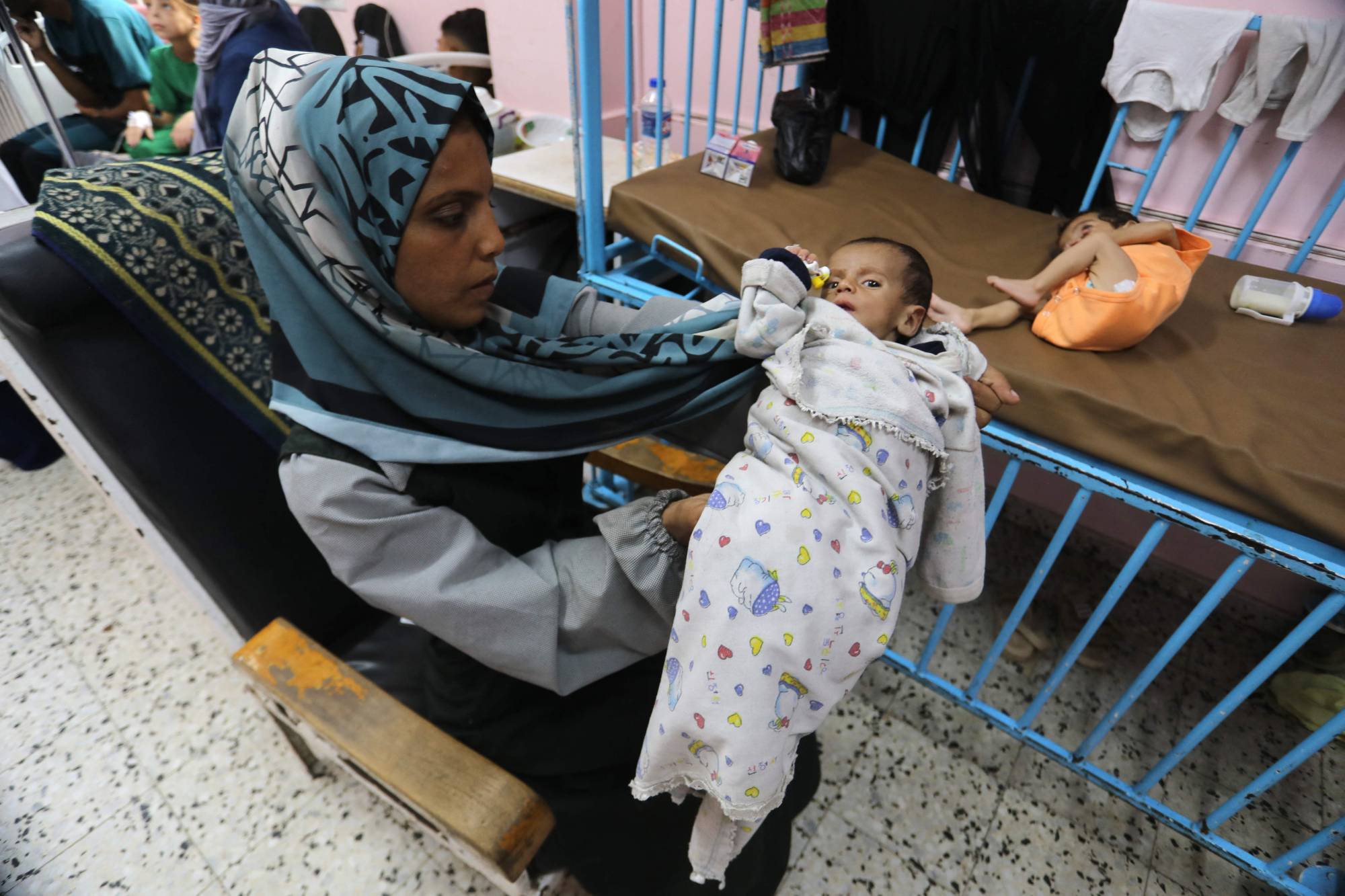 فلسطينية تحمل رضيعها المصاب بسوء تغذية كبير في مستشفى ناصر بخان يونس جنوب قطاع غزة الخميس الماضي (أ.ف.ب)