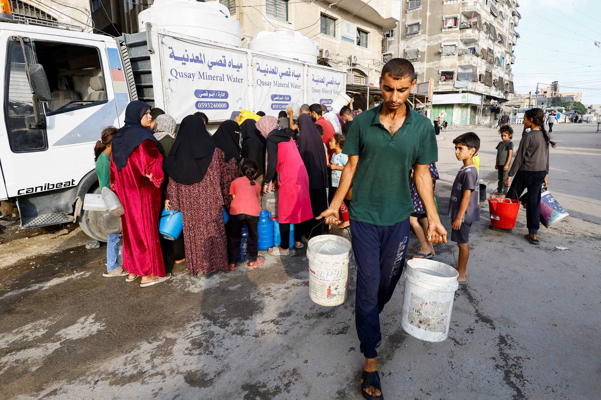 فلسطيني يحمل دلوَي ماء فيما ينتظر آخرون لتعبئة بعض المياه بمدينة غزة وسط شح حاد يوم الأربعاء (رويترز)