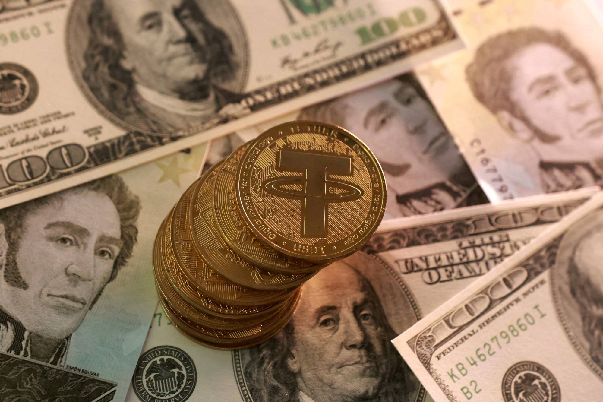 أوراق نقدية وهمية من الدولار الأميركي والبوليفار الفنزويلي ورموز للعملة المشفرة تيثر (رويترز)