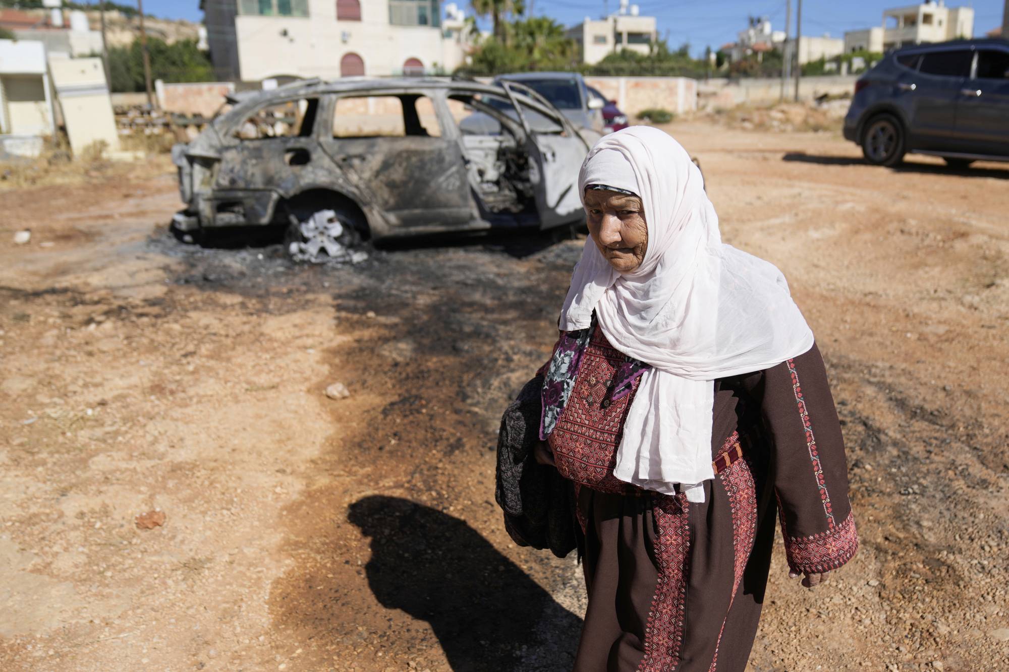 امرأة تمر أمام سيارة أحرقها مستوطنون إسرائيليون طوال الليل في الضفة الغربية (أ.ب)