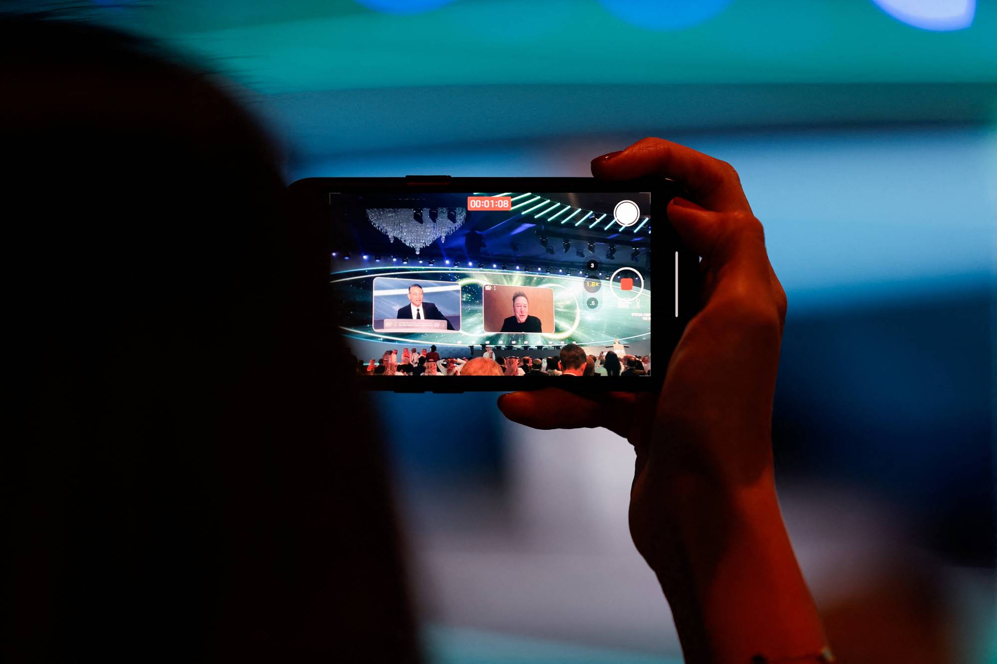 امرأة تستخدم هاتفاً لتسجيل كلمة الرئيس التنفيذي لشركة «تسلا» إيلون ماسك خلال النسخة الثامنة من المؤتمر (رويترز)