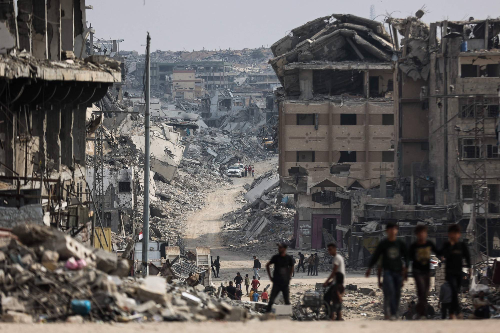 فلسطينيون يسيرون قرب منطقة يجري فيها البحث عن جثث رهائن إسرائيليين وسط الأنقاض بمدينة غزة يوم الاثنين (أ.ف.ب)