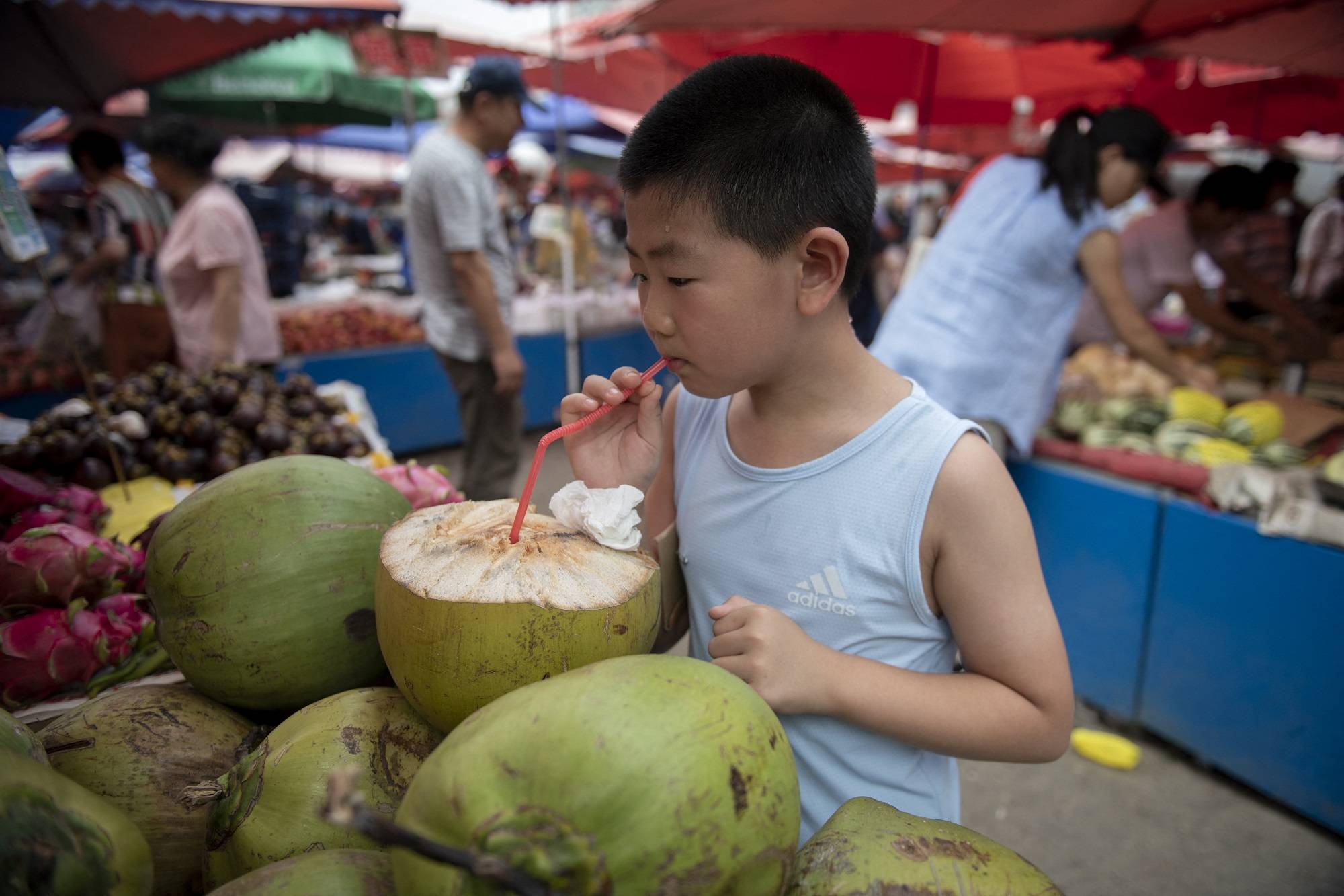 صبي يشرب ماء جوز الهند الطازج في إحدى أسواق بكين (أ.ف.ب)