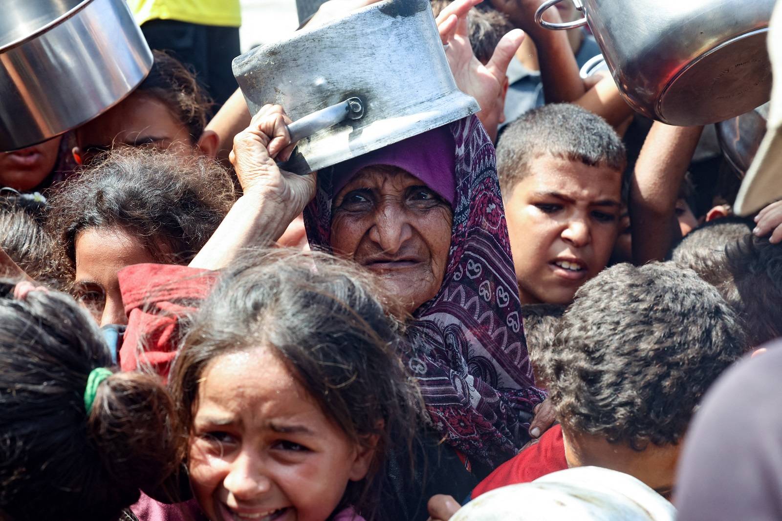 Han Yunus'ta bir yardım kuruluşunun aşevinden yiyecek almak için çocuklarla birlikte bekleyen yaşlı bir Filistinli kadın (AFP)
