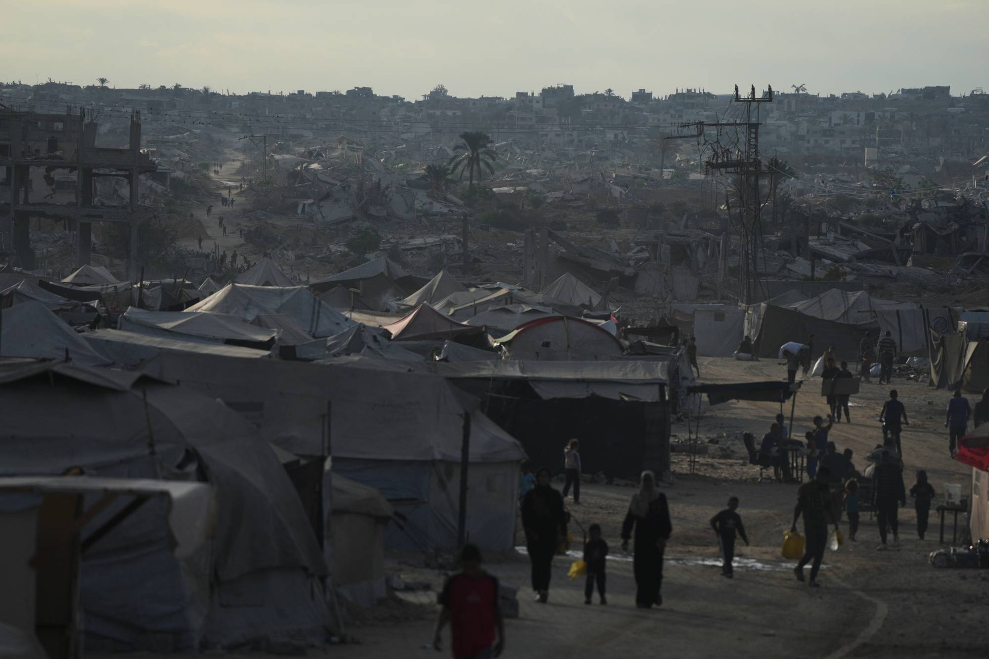  Gazze Şeridi'nin Han Yunus kentinde yıkılmış ev ve binaların yanındaki çadır kampından geçen yerlerinden edilmiş Filistinliler, 18 Ekim 2025 (AP)