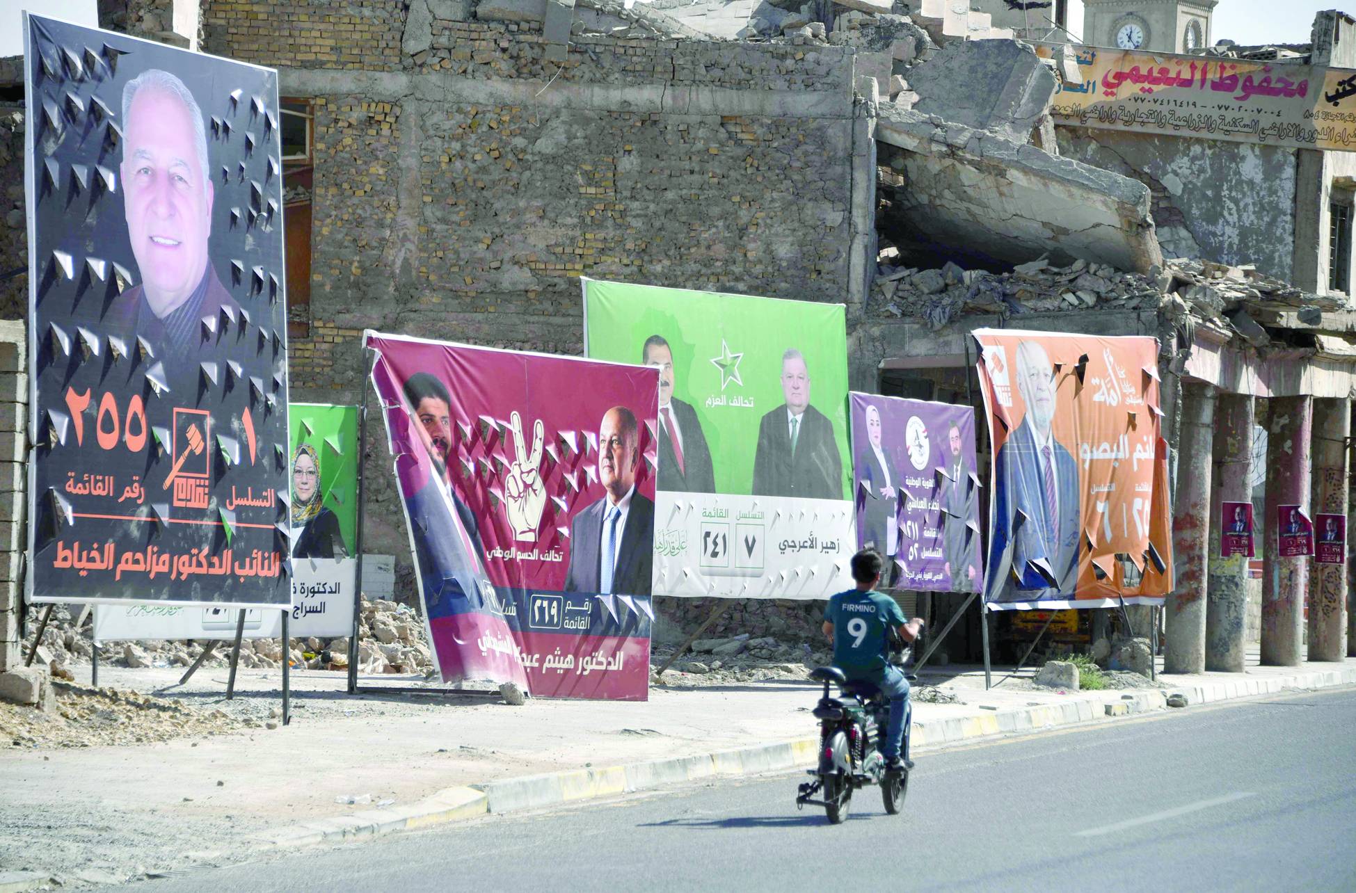 Musul’daki aday afişlerinin önünden elektrikli bisikletiyle geçen bir genç (AFP)