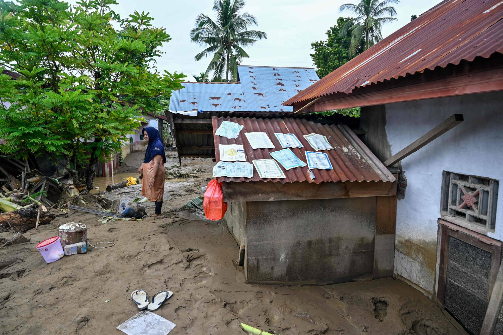 Endonezya'nın Açe eyaletine bağlı Pidie Jaya bölgesindeki Miurido'da meydana gelen ani sel felaketinin ardından bir sakin derin çamurun üzerinden bakarken, bir evin çatısında kuruyan belgeler (AFP)
