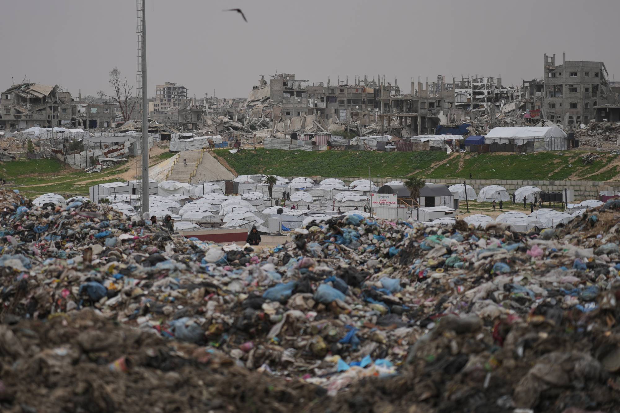 İsrail saldırılarının ardından oluşan yıkımın ve Han Yunus'taki çöp yığınının ortasında, yerinden edilmiş Filistinlilere barınak sağlayan çadırlar görünüyor. (AP)