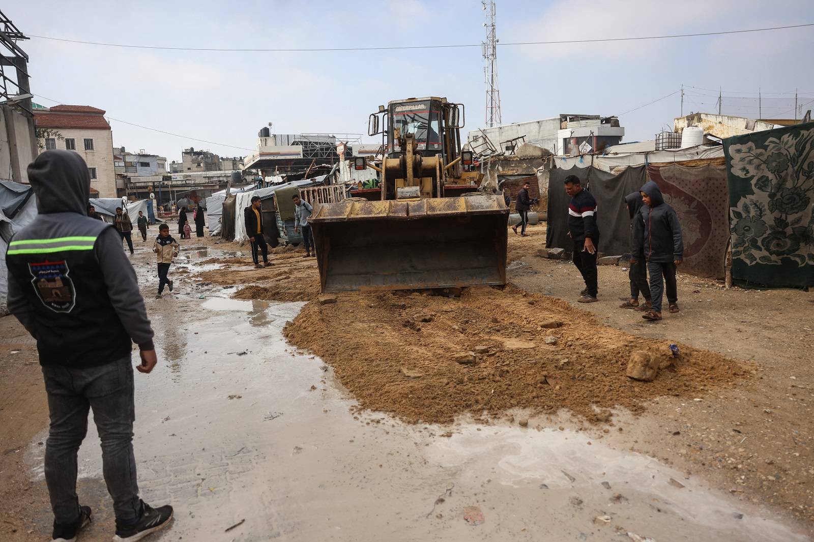 Gazze Şeridi'nin güneyindeki Han Yunus'ta Filistinli mültecileri barındıran geçici bir kampta yağmur nedeniyle su basan bir caddeden suyu tahliye etmeye çalışan bir buldozer (AFP)