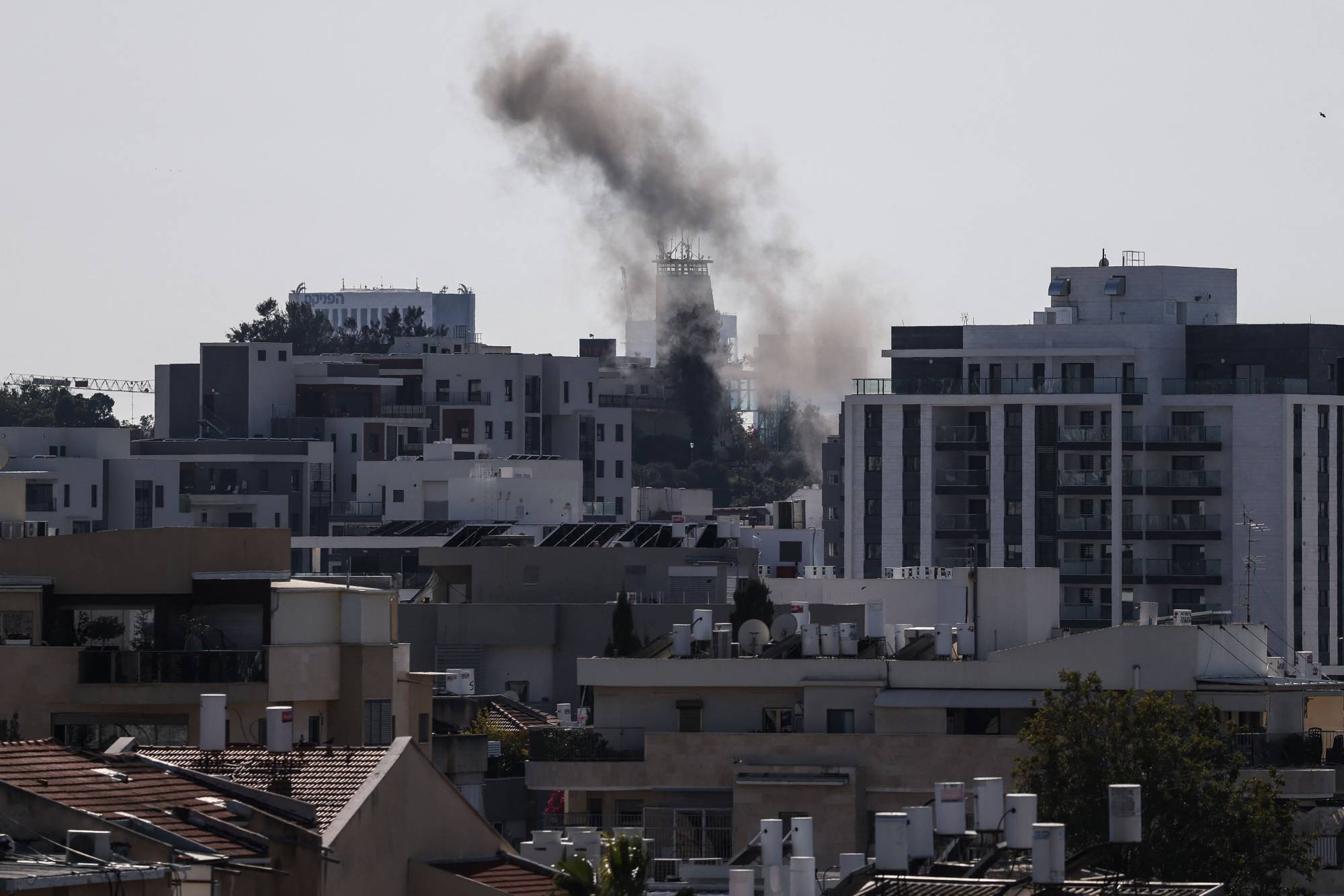 Tel Aviv'de bir merminin bölgeye isabet etmesinin ardından binaların arkasından duman yükseliyor (AFP)