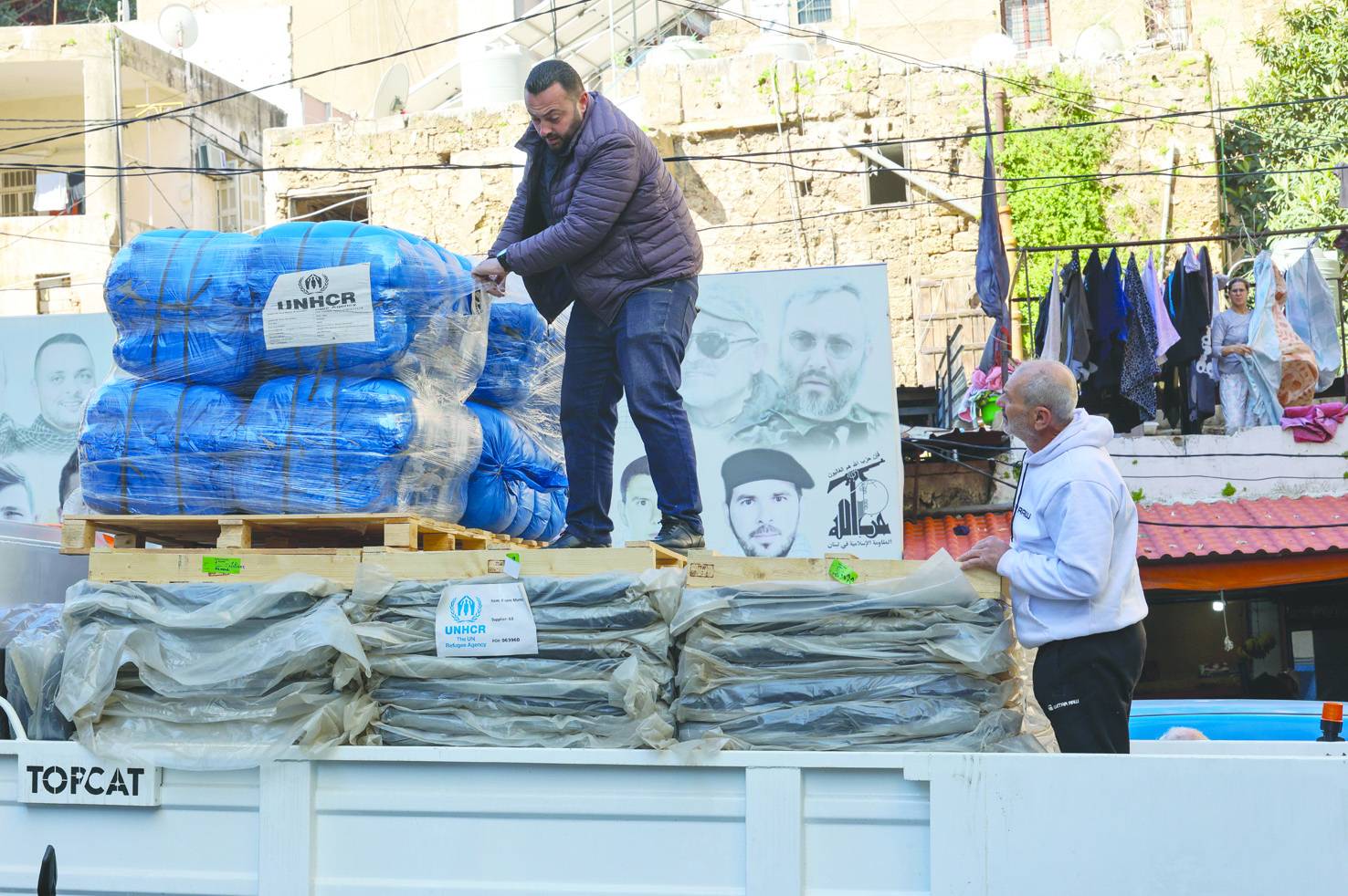 Beyrut’ta sığınağa dönüştürülen bir okulda battaniye dağıtımı... Arka plandaki fotoğrafta Hizbullah liderleri ve üyeleri görülüyor (EPA)