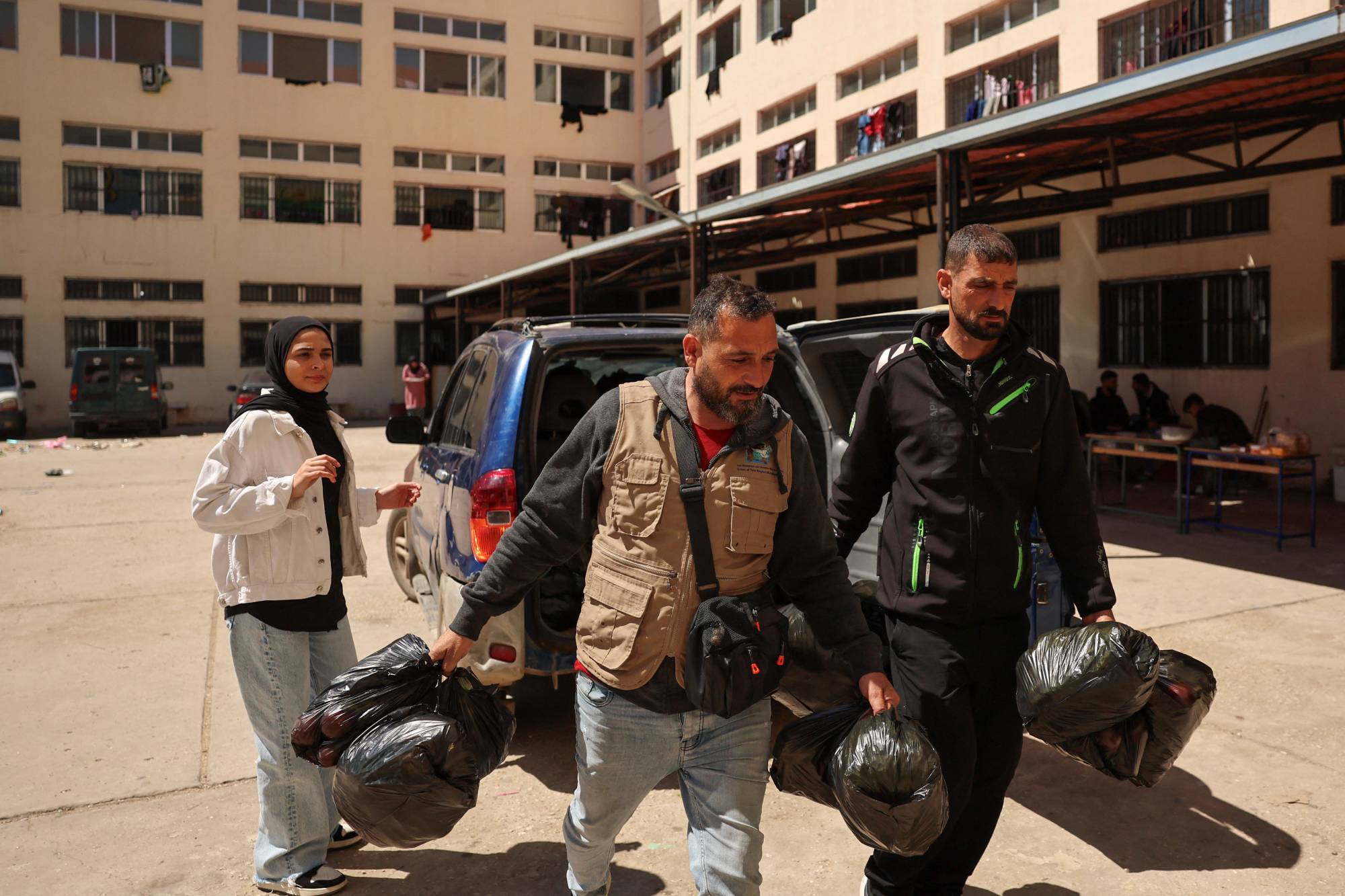 İki gönüllü, Lübnan'ın güneyindeki Sur (Tire) şehrinde yerinden edilmiş insanlara dağıtılmak üzere meyve ve sebze dolu çuvallar taşıyor (Reuters)