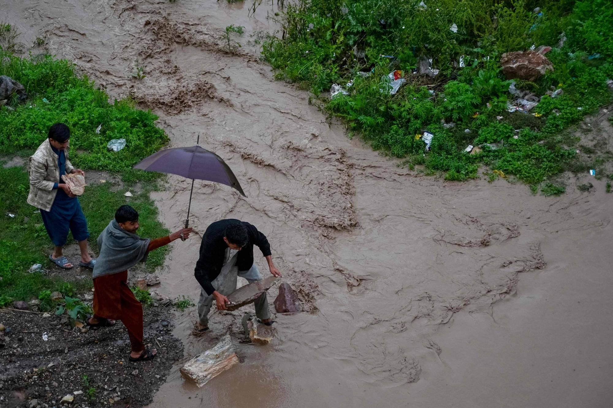  Pakistan'ın Peşaver kentinde, şiddetli yağmurların ardından bir drenaj kanalının taşması sonucu sular altında kalan yolda, sakinler taş kullanarak karşıya geçiyor (AFP)