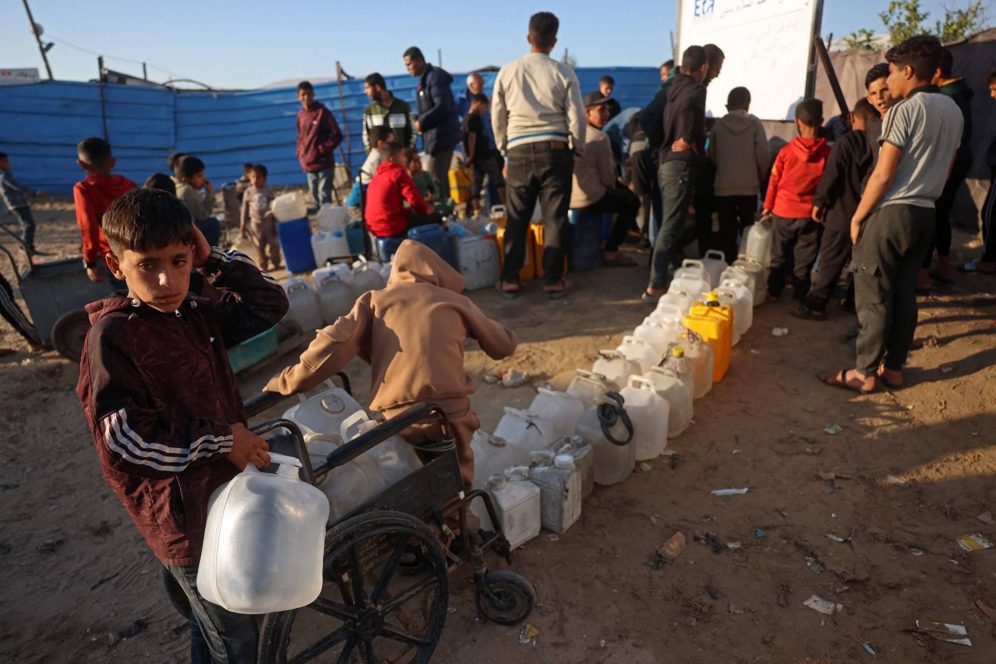 Gazze Şeridi’nin güneyindeki Han Yunus’ta bulunan bir mülteci kampında su kaplarını doldurmak için bekleyen Filistinliler, 10 Nisan 2026 (AFP)