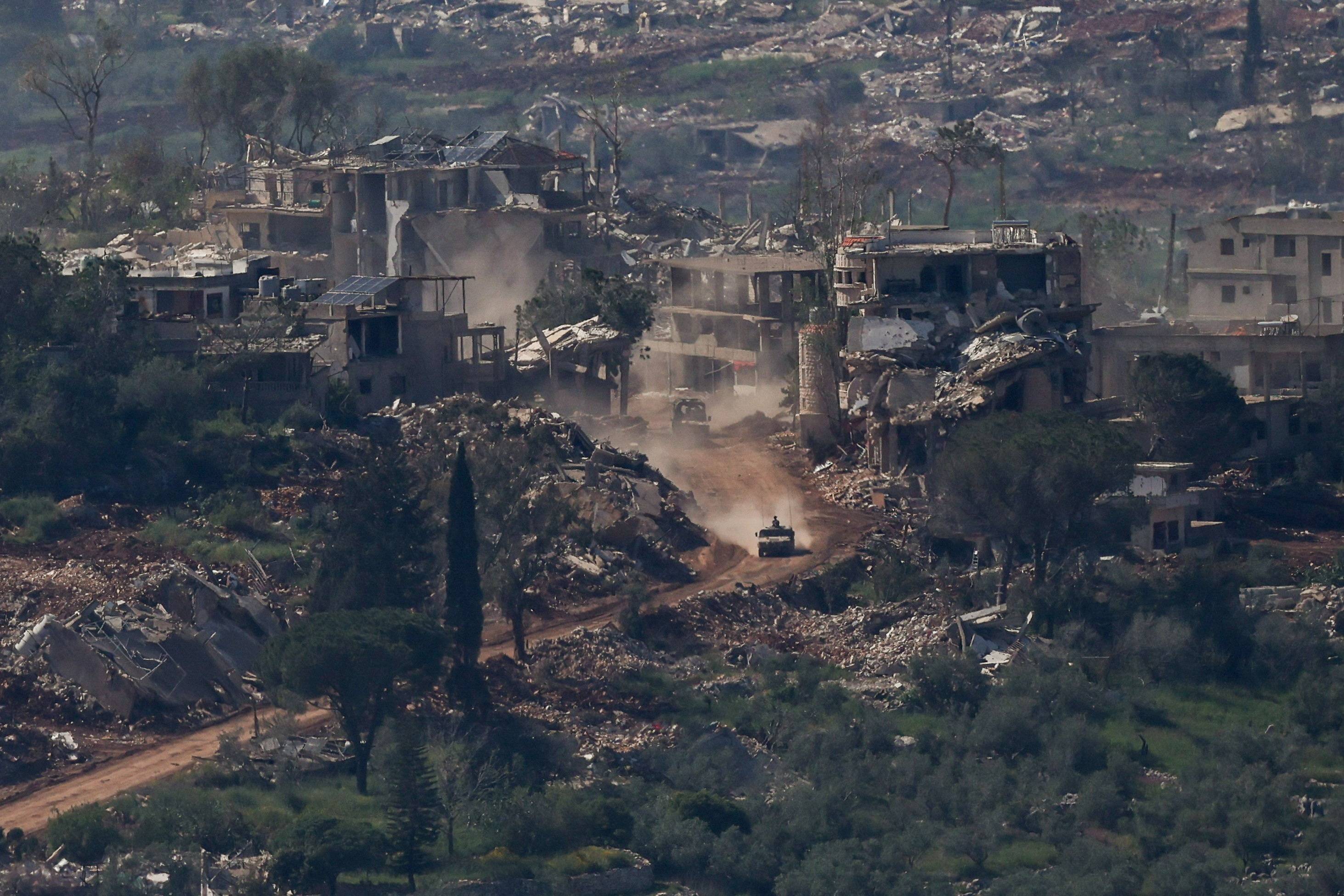  İsrail'e ait bir askeri araç, Lübnan toprakları içindeki yıkılmış binaların yanından geçiyor (Reuters).