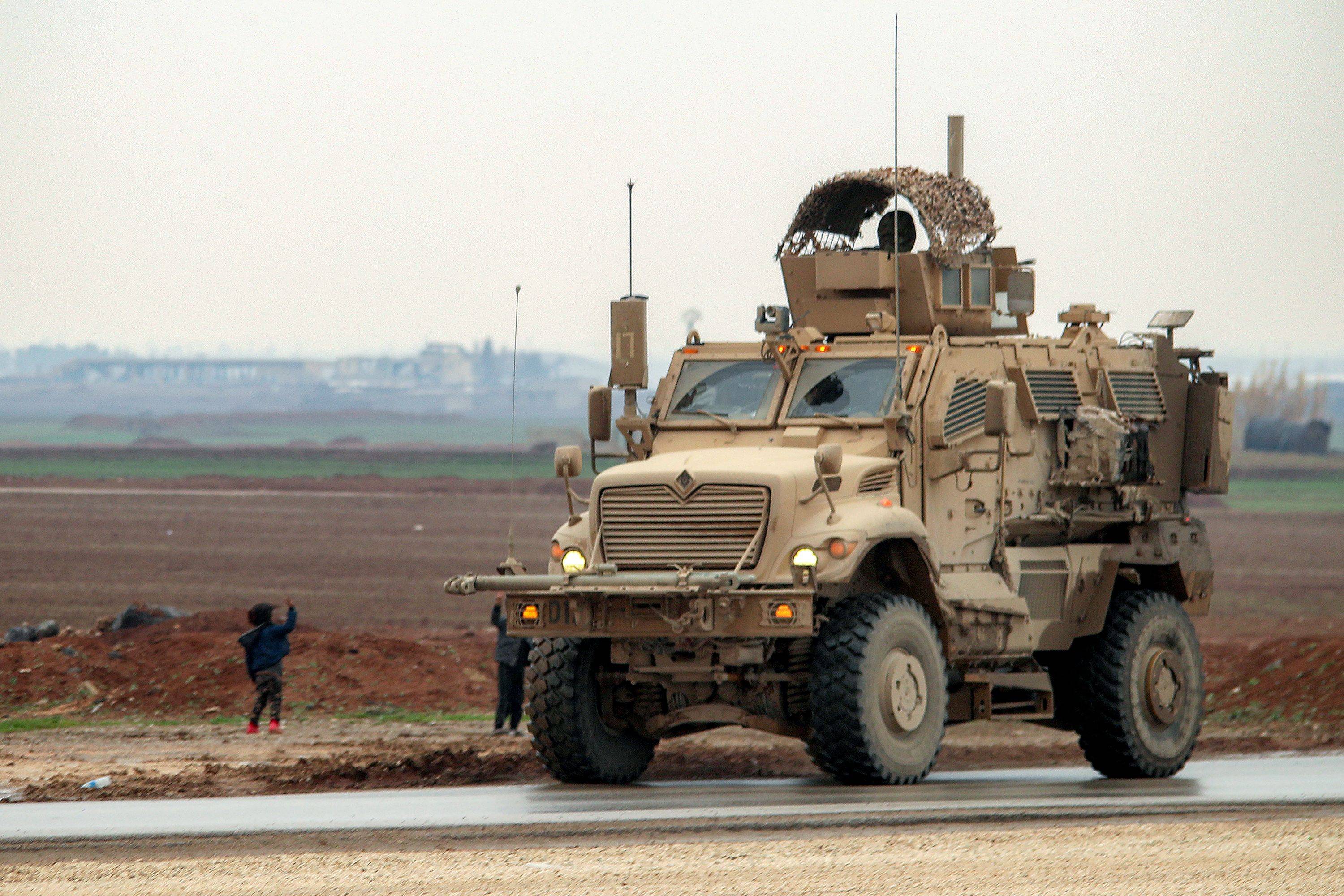  7 Şubat'ta Suriye'nin kuzeydoğusundaki el-Haseke'nin el-Kahtaniye banliyölerinde, DEAŞ tutuklularını Suriye'den Irak'a taşıyan bir konvoydaki çocuklar, Amerikan yapımı zırhlı bir araca el sallıyor (AFP)