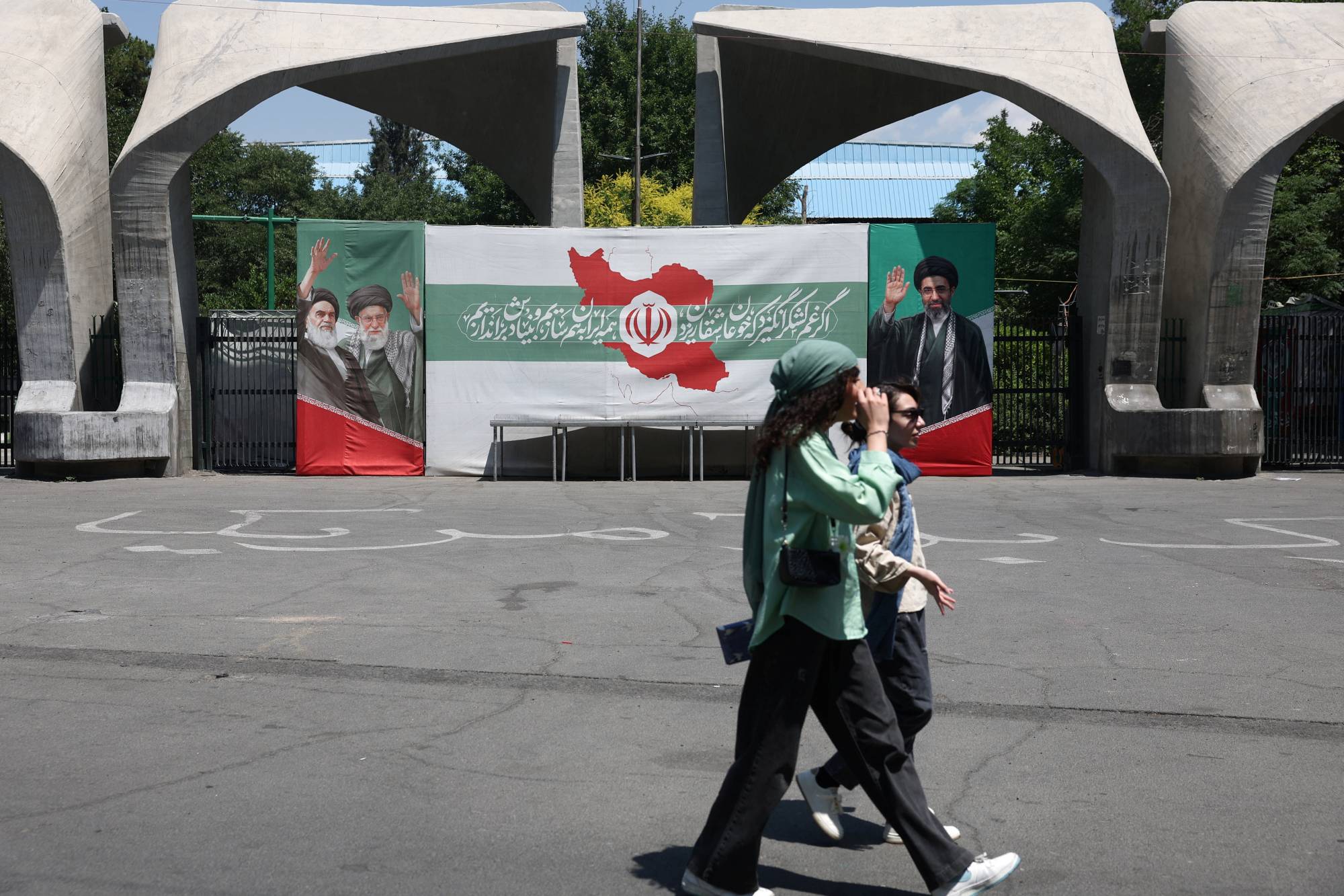 3 Haziran 2026’da Tahran Üniversitesi girişinde, Humeyni, Ali Hamaney ve Mücteba Hamaney’in fotoğraflarının yer aldığı bir pankartın önünden geçen İranlı kadınlar (Reuters)