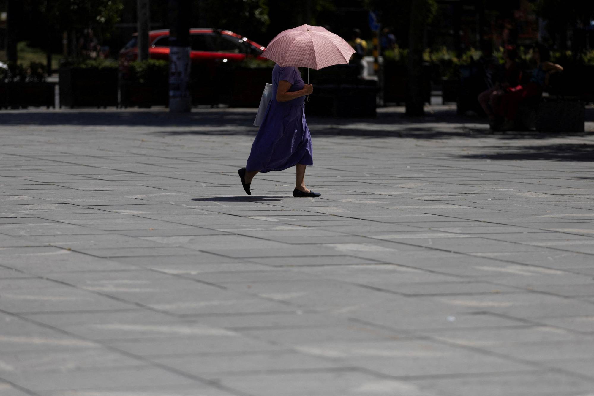 Belgrad'da sokakta yürürken şemsiye ile güneşten korunan bir kadın (Reuters)