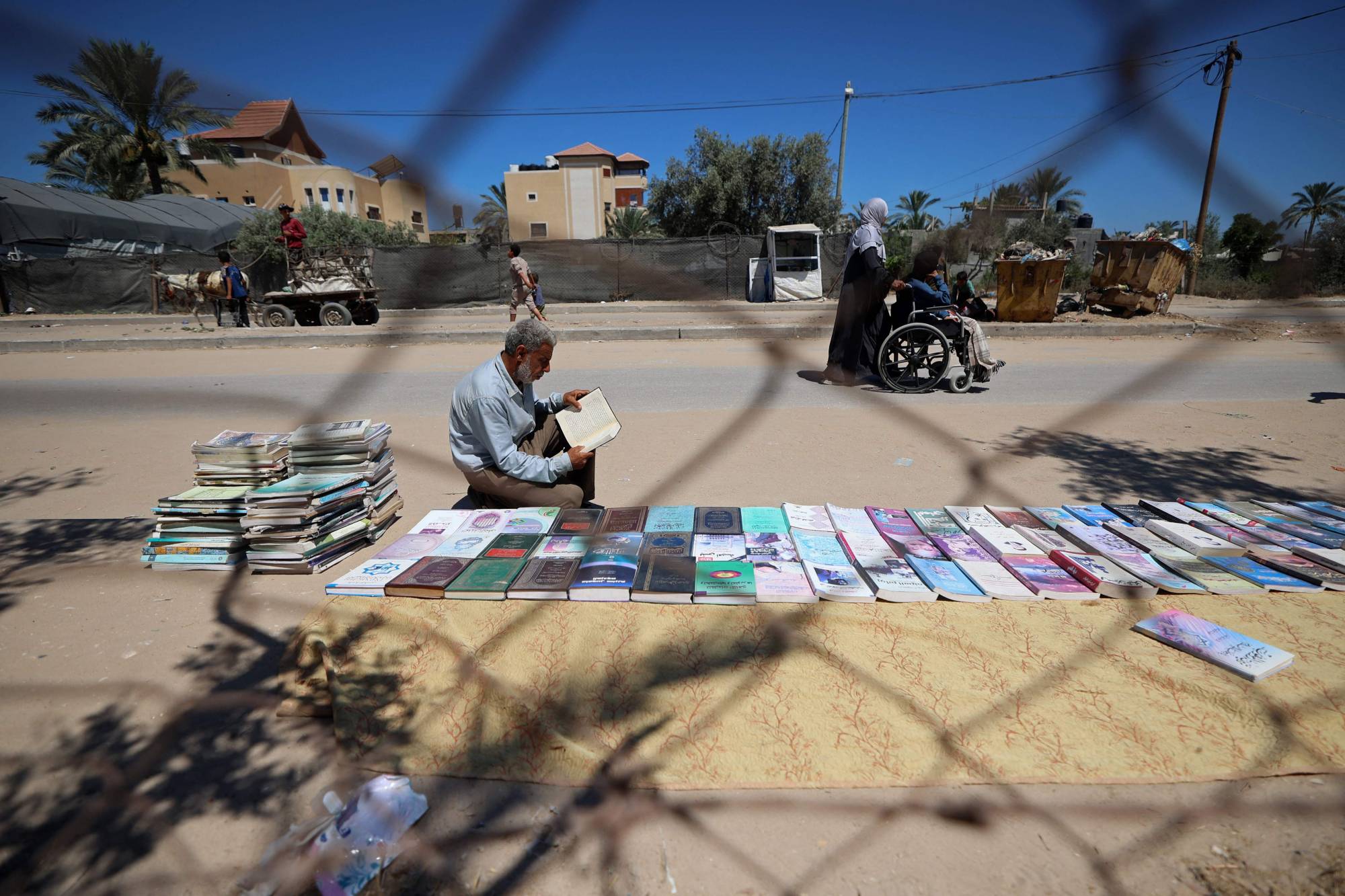 Yerinden edilen bir sahaf, Gazze Şeridi'nin orta kesimindeki Deyr el-Belah'ta kaldırım üzerinde kitap satıp kiralıyor. (AFP)