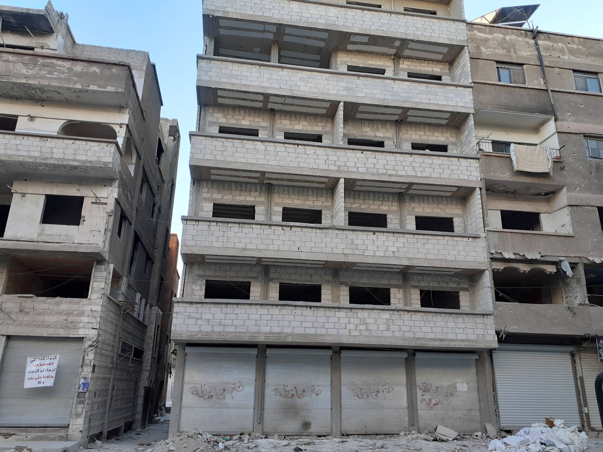 Yeniden inşa edilmiş bir bina ve dükkanların kapılarında Şam Valiliği mührü görülüyor (Şarku’l Avsat)