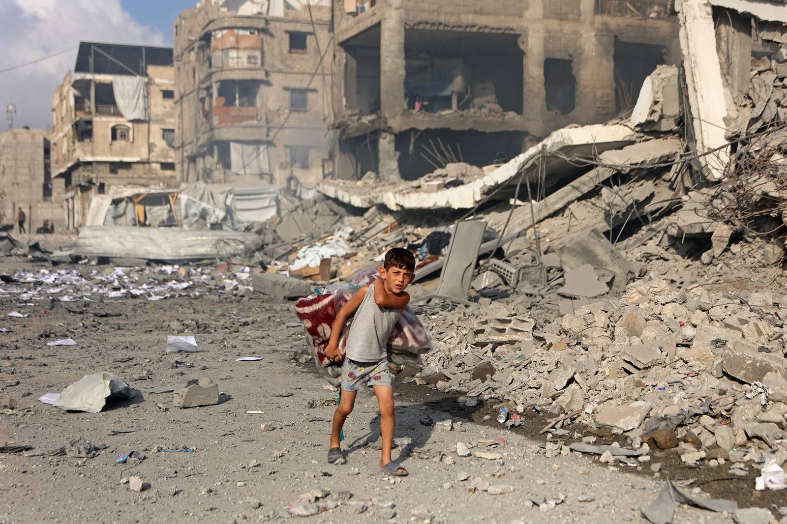 İsrail’in Gazze kentinde düzenlediği hava saldırısının ardından yıkılan binaların yanında yürüyen Filistinli çocuk (AFP)