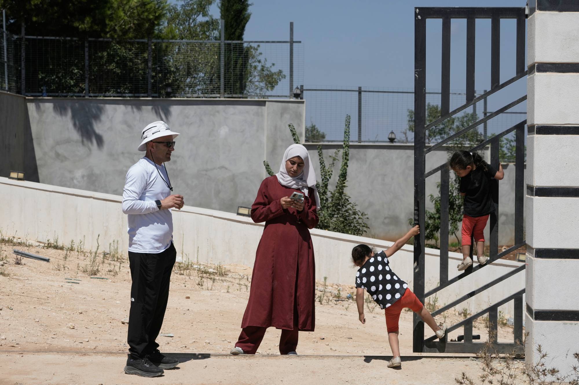 Filistin asıllı Amerikalı vatandaş Louay Reddy, eşi ve iki kızıyla birlikte, etrafı İsrailli yerleşimcilerle çevrili evinin bahçesinde (AP)