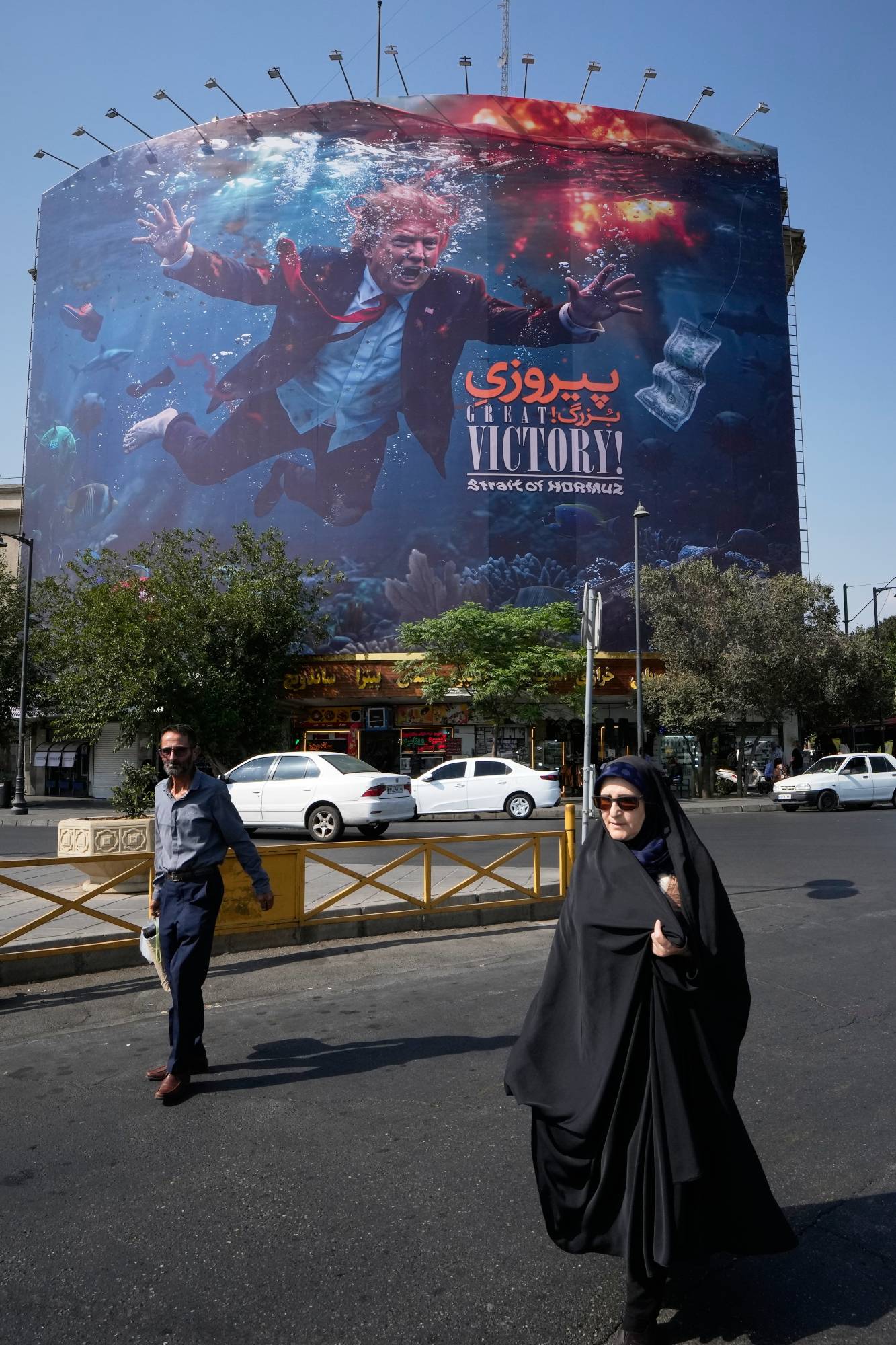 Yayaların, Tahran'da ABD Başkanı Donald Trump'ı patlamalar arasında su altında gösteren ve üzerinde “Büyük zafer! Hürmüz Boğazı” yazan bir reklam panosunun önünden geçişi, 24 Ağustos 2026 Pazartesi (AP)