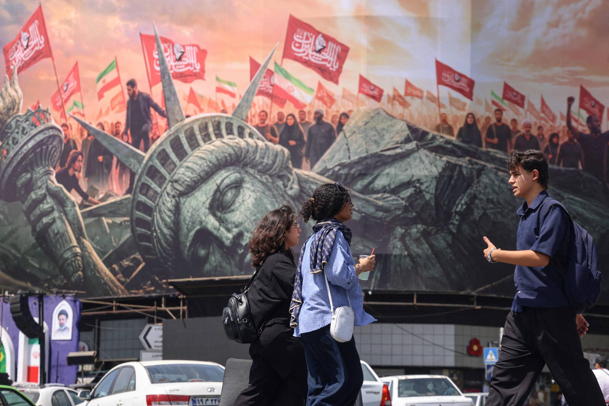 İnsanlar, 2 Eylül 2026’da Tahran’ın merkezindeki İnkıllap Meydanı’nda ABD karşıtı bir reklam panosunun önünden geçiyor. (AFP)