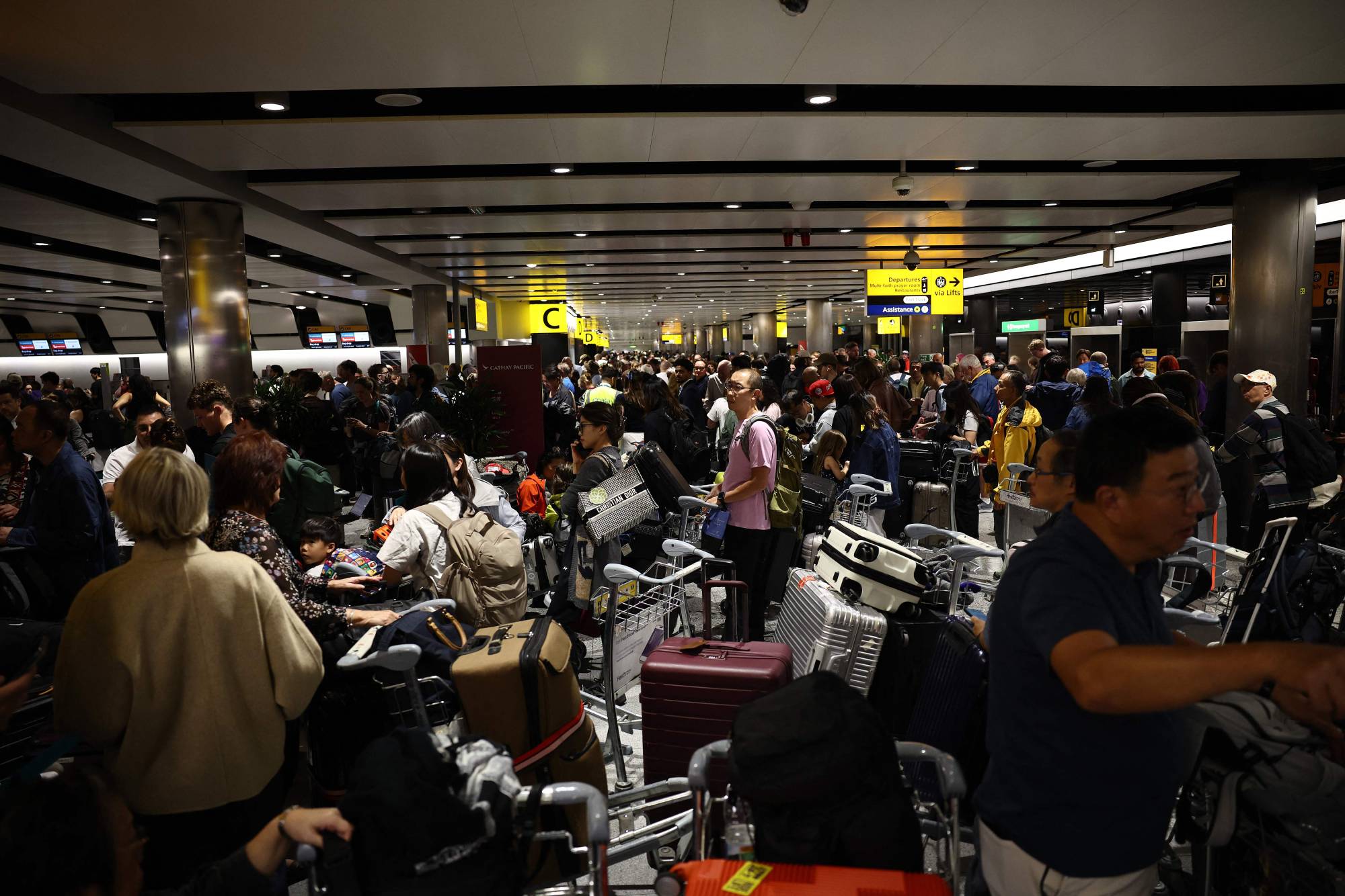 Uçuşları geciken yolcular, Londra’nın batısındaki Heathrow Havalimanı’nın 3 numaralı terminalinde bagajlarıyla bekliyor ve kuyruk oluşturuyor. (AFP)