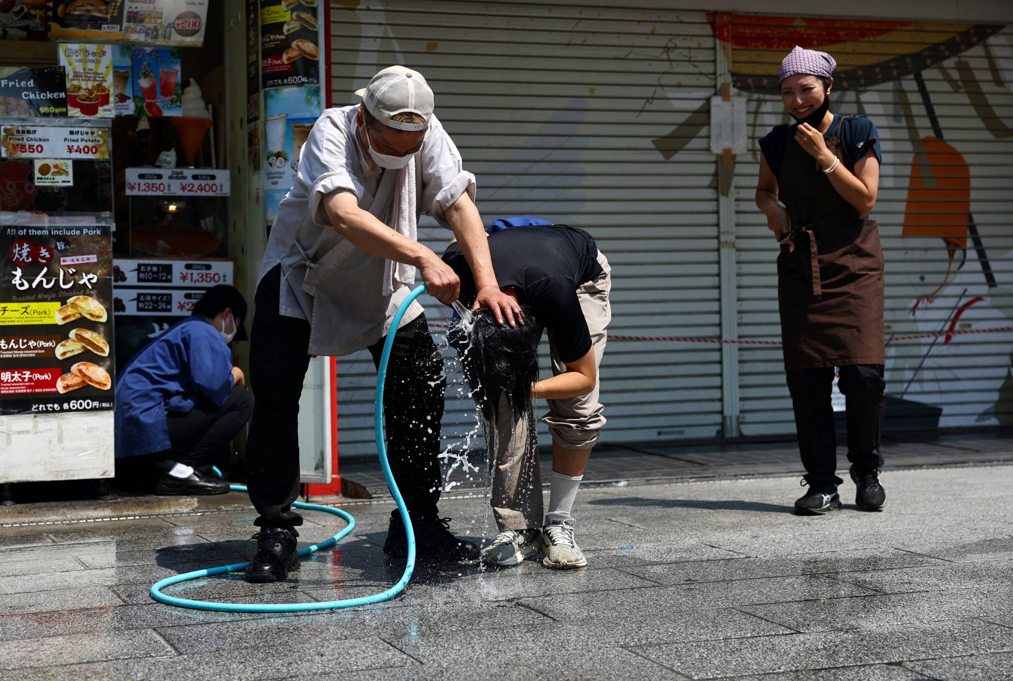 Tokyo’da şiddetli sıcak hava dalgası sırasında 22 Temmuz 2026’da bir fast-food restoranı çalışanı, başına su dökerek bir kişiyi serinletmeye çalışıyor (Reuters)