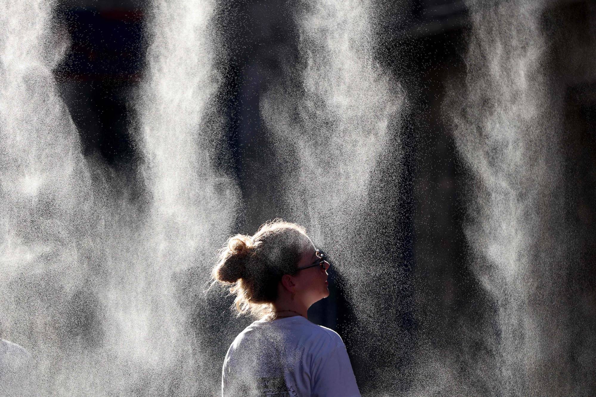 Fransa’nın güneybatısındaki Bordeaux kentinde, sıcak hava dalgası sırasında düzenlenen bir müzik festivali esnasında su püskürtülen bir alanda serinleyen kadın (AFP)