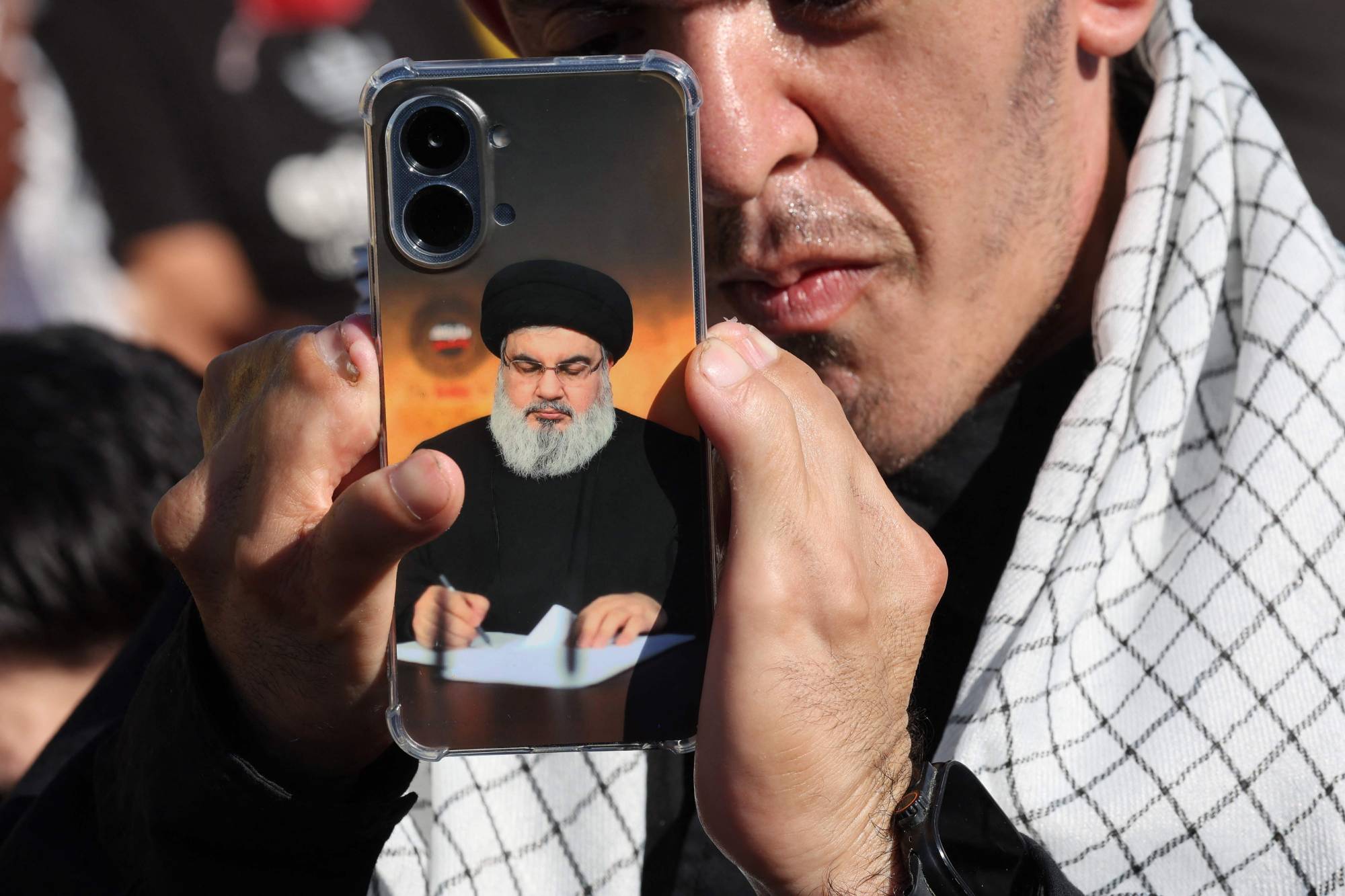 Çağrı cihazı patlamalarında yaralanan bir Hizbullah mensubu, eski Genel Sekreter Hasan Nasrallah’ın fotoğrafının bulunduğu telefonu, Nasrallah’ın öldürülmesinin ikinci yıl dönümü anmasında taşıyor (AFP)