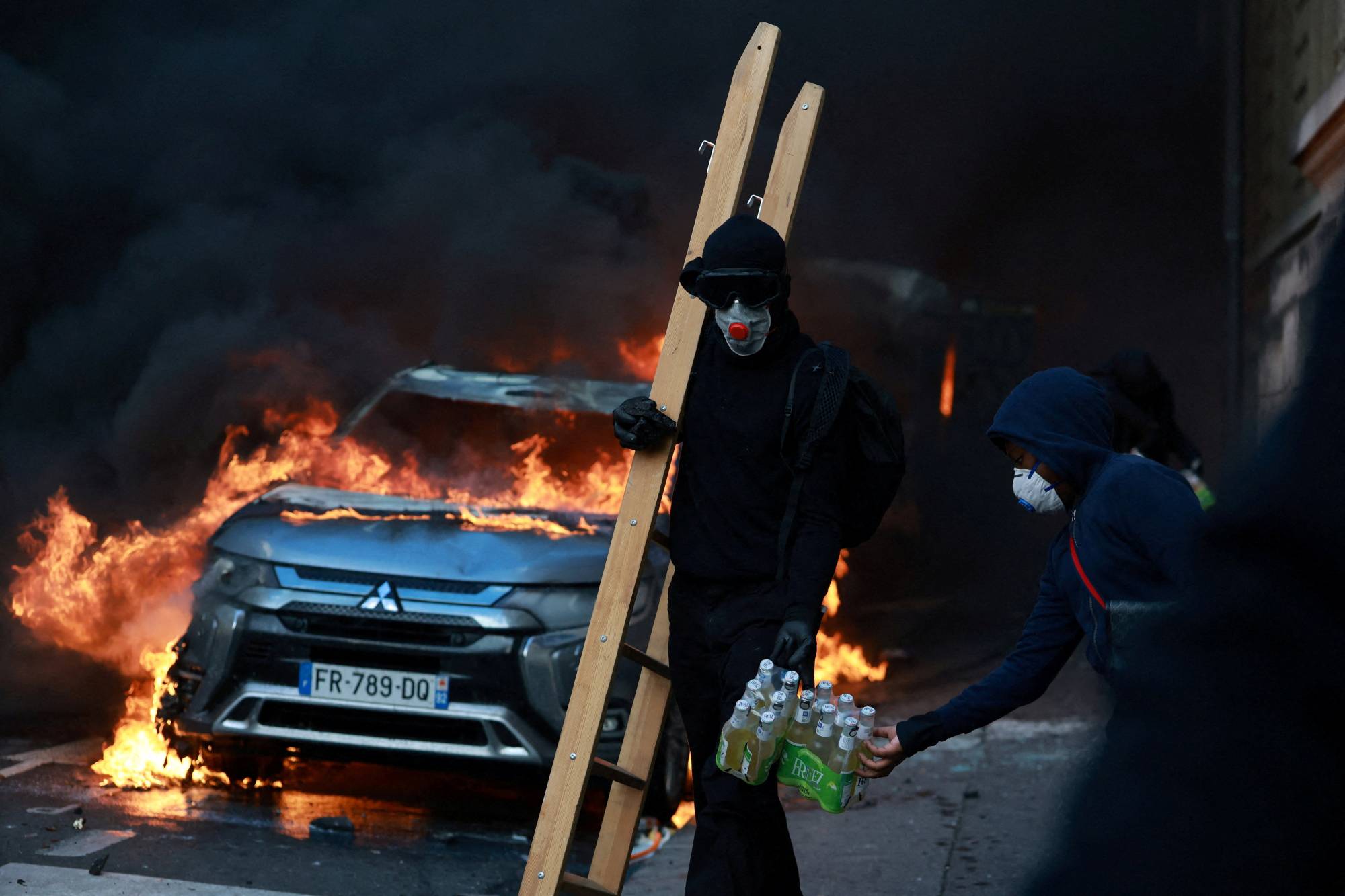 Paris’te, Cumhuriyet Meydanı yakınlarında hayat pahalılığı ve artan akaryakıt fiyatlarına karşı düzenlenen protestolardaki çatışmalar sırasında, maskeli bir gösterici yanan bir aracın yanından geçerken görüntülendi. (Reuters)