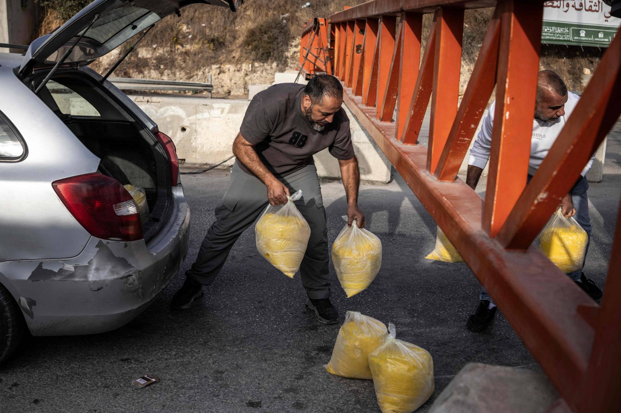 İşgal altındaki Batı Şeria’nın El Halil kentinde, cumartesi günü kapalı bir İsrail kontrol noktasının altından poşet geçiren iki Filistinli. (AFP)