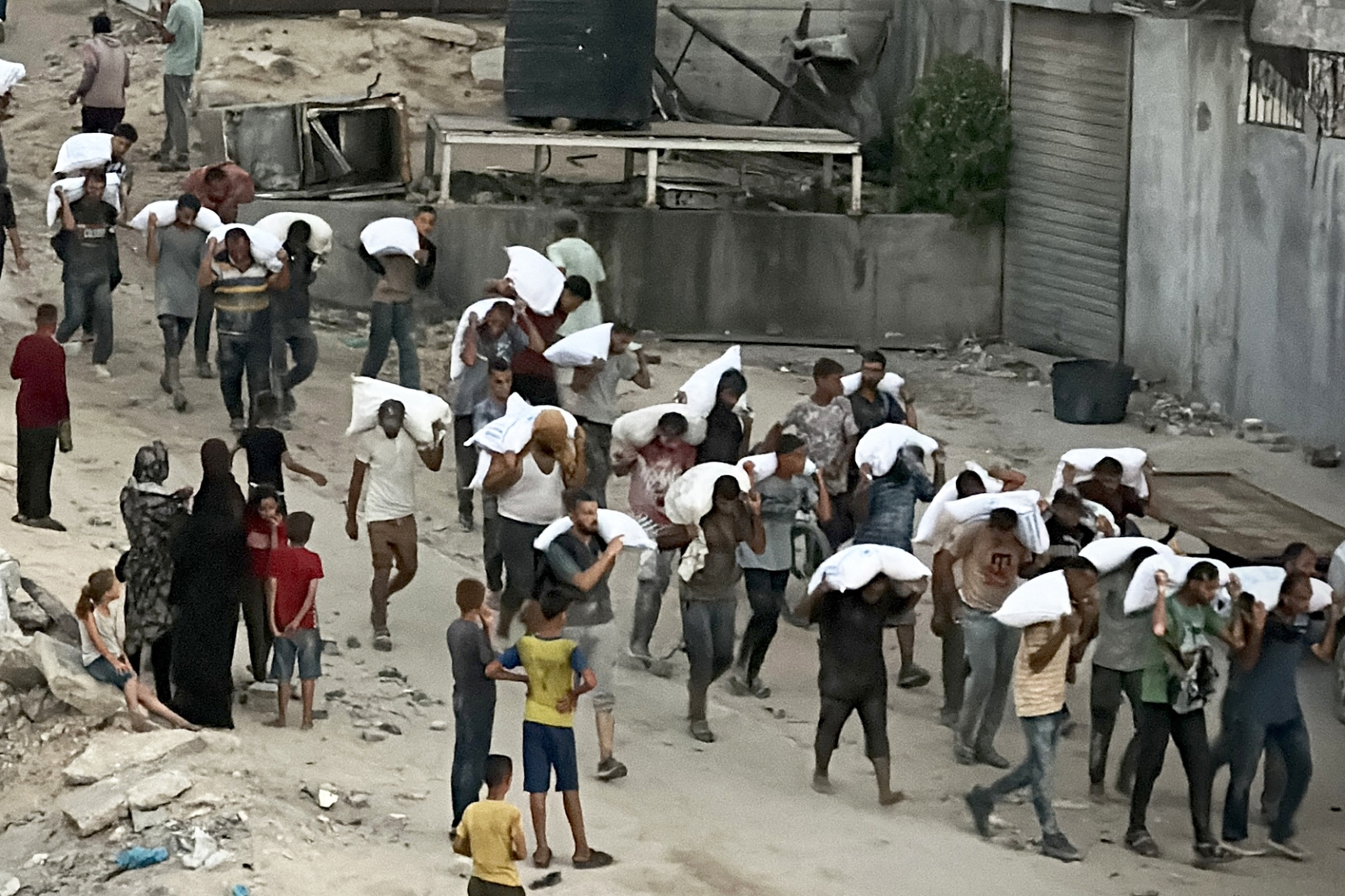  Gazze Şeridi'nin güneyindeki Han Yunus'ta gıda malzemesi taşıyan bir kamyona baskın düzenlendikten sonra un çuvallarını taşıyan adamlar, 22 Temmuz 2025 (AFP)