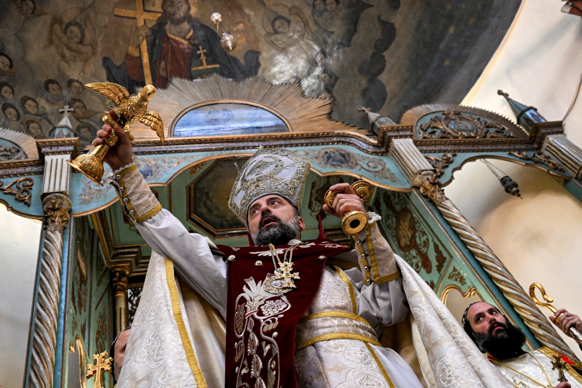 Şam Ermeni Apostolik Kilisesi Piskoposu Armaş Nalbandyan, eski Şam bölgesindeki Bab el-Şarki'de bulunan Aziz Sarkis Kilisesi'nde düzenlenen Noel Ayini'nde su kutsaması sırasında bir güvercin heykelini tutuyor, 6 Ocak 2025 (AFP)