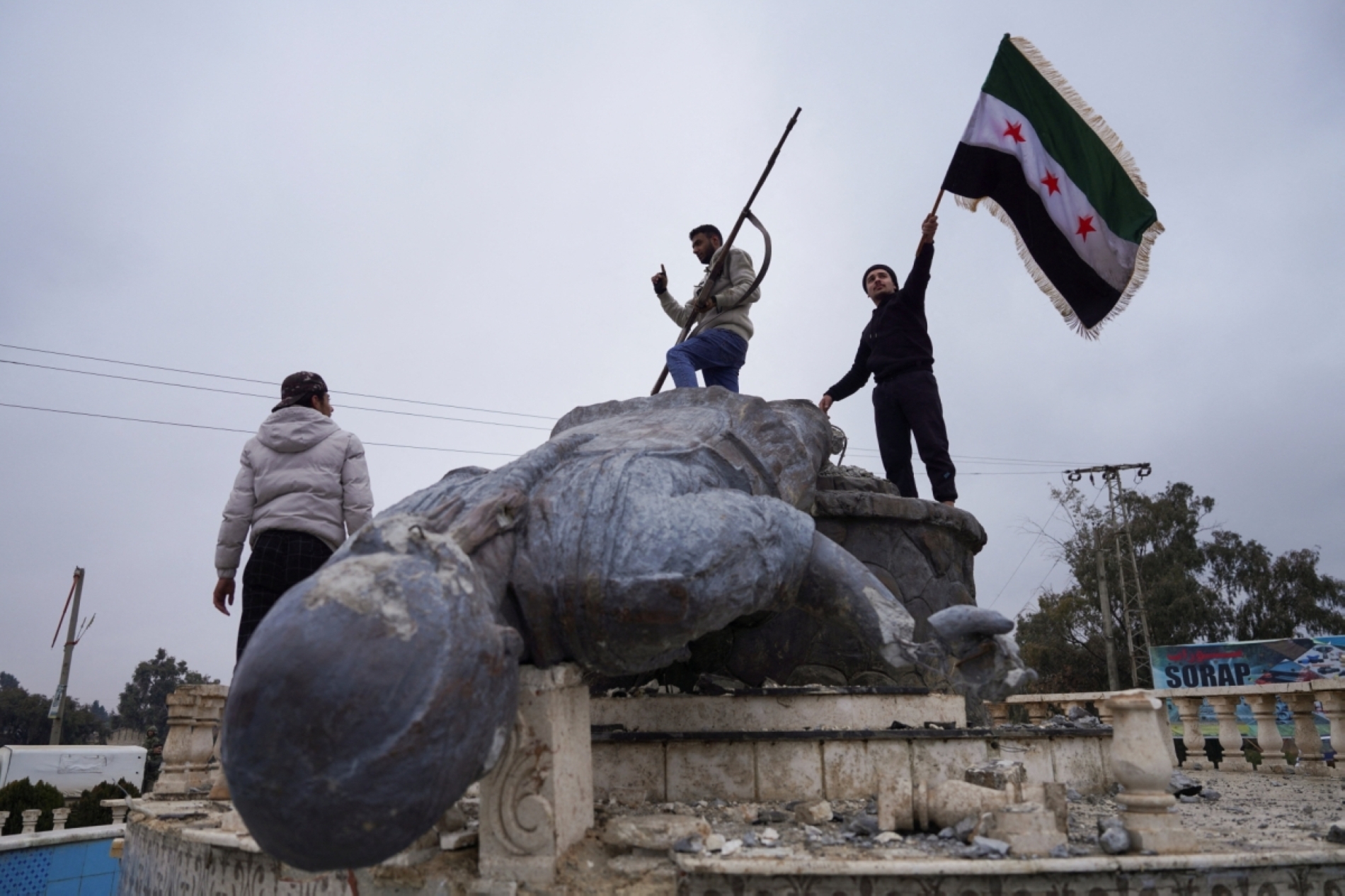 Suriye'nin kuzeydoğusundaki Tabka'da, SDG’li bir kadın savaşçının parçalanmış heykelinin üzerine çekilen Suriye bayrağı, 18 Ocak 2026 (Reuters)
