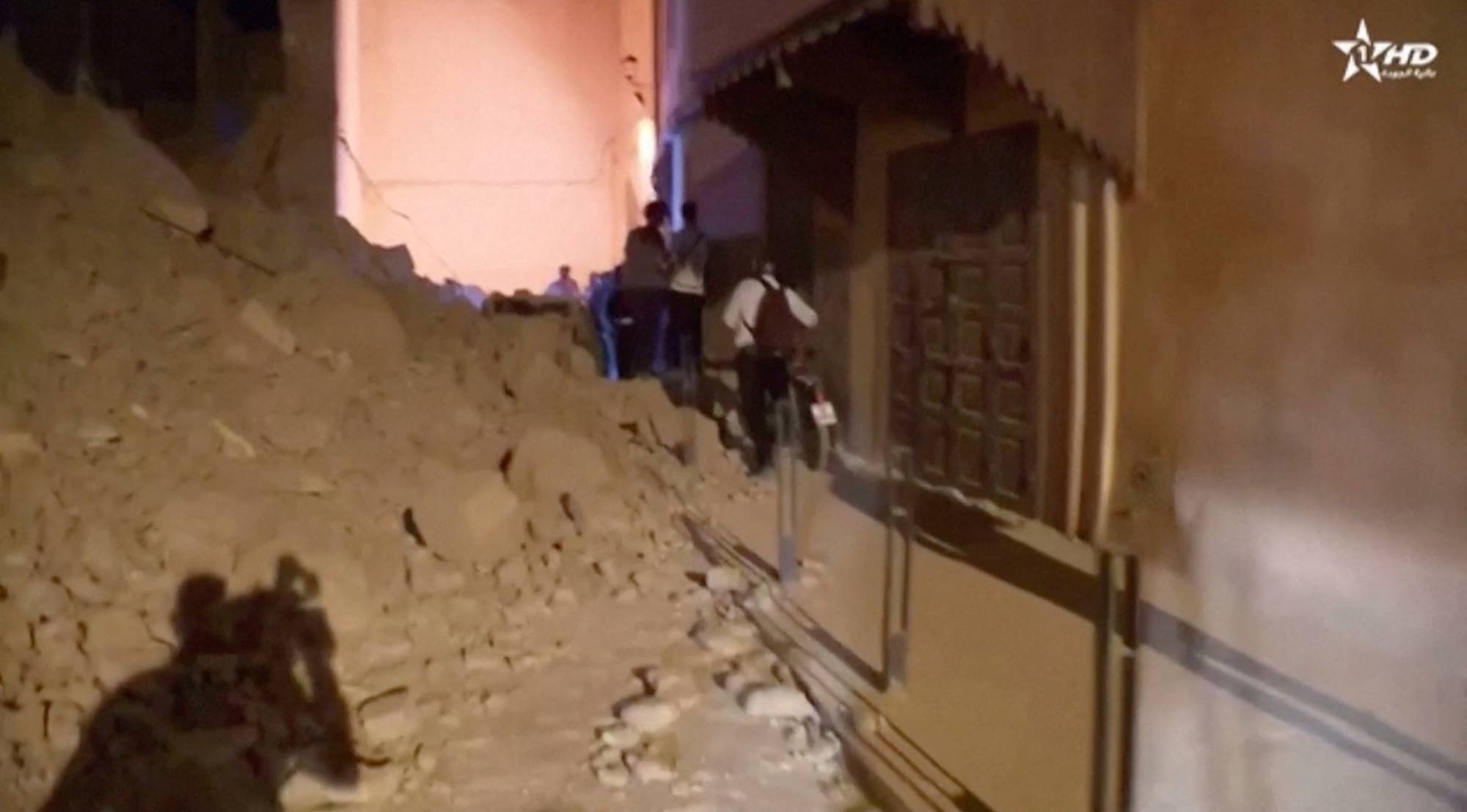 Marakeş'te meydana gelen depremin enkazının yakınında yürüyen insanları gösteren bir haber yayınından görüntü (Reuters)
