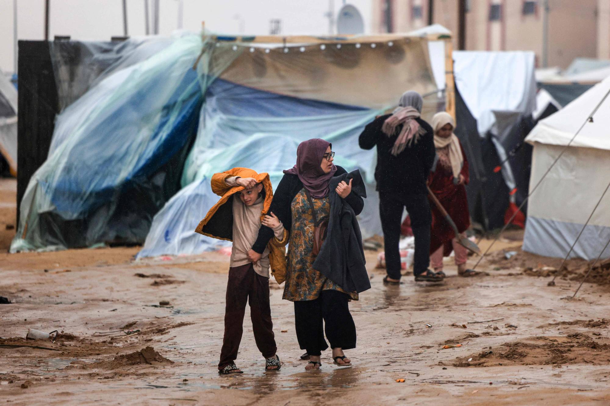 FOTO: Filistinliler, Gazze Şeridi’nin güneyindeki Refah’ta yerlerinden edilmişlere yönelik bir kampta yağmur altında yürüyor (AFP)