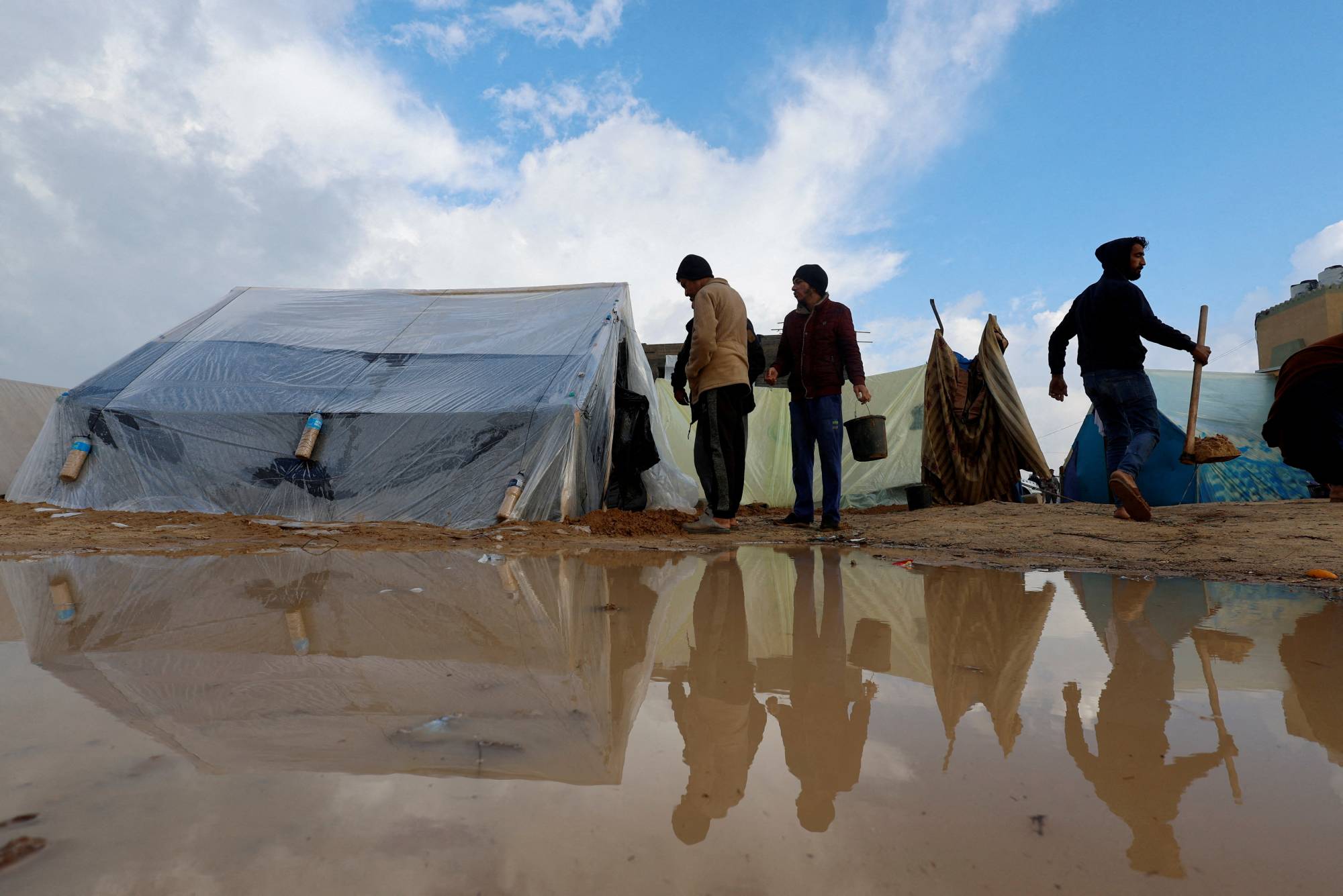 FOTO: İsrail’in saldırıları nedeniyle evlerinden kaçan Filistinliler, mülteci kamplarındaki şiddetli yağışların ardından çadırların yanında yürüyor (Reuters)
