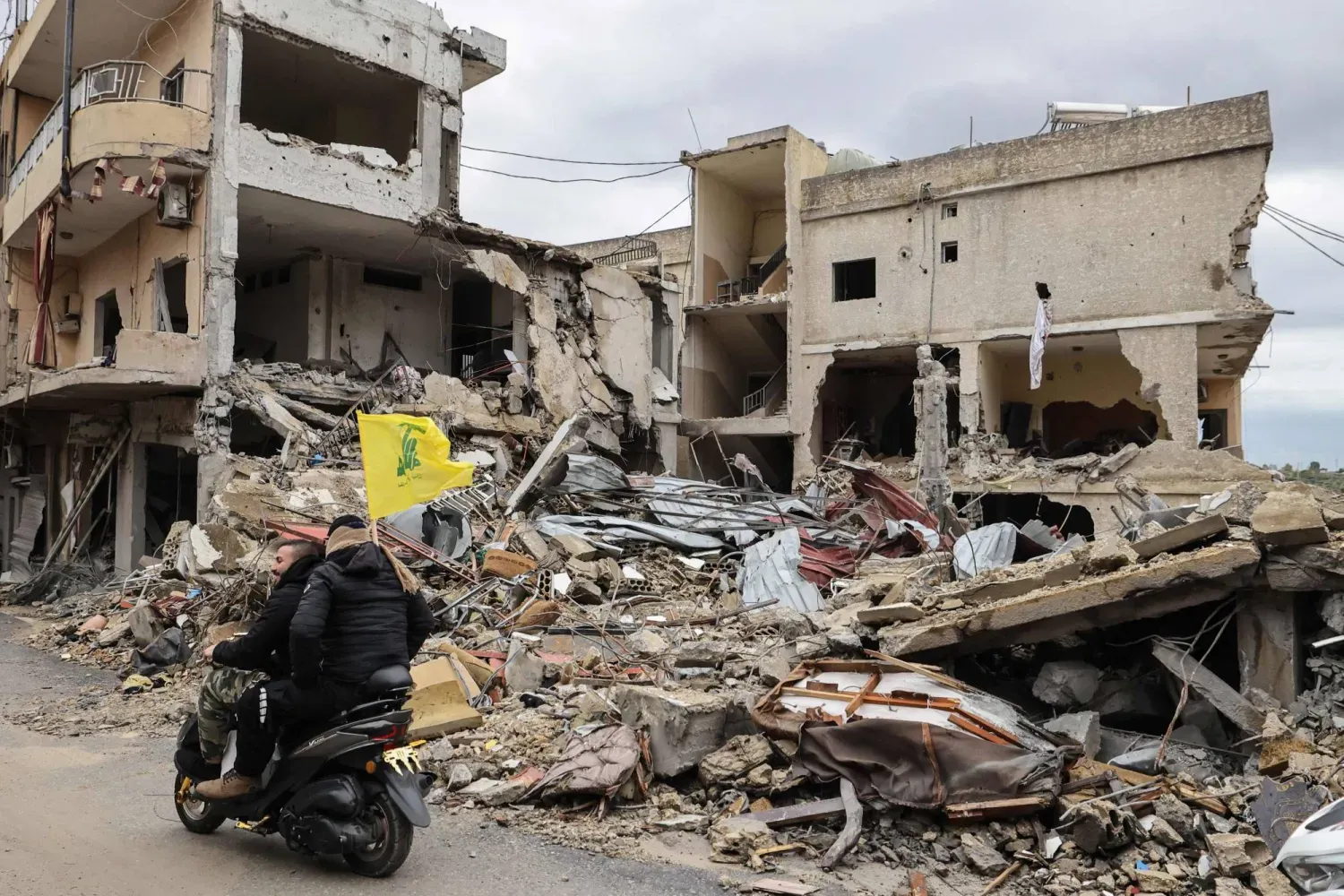 Lübnan'ın güneyinde insanlar evlerine doğru ilerlerken Hizbullah bayrağı taşıyan bir motosikletli adam yıkılmış binaların yanından geçiyor (AFP)