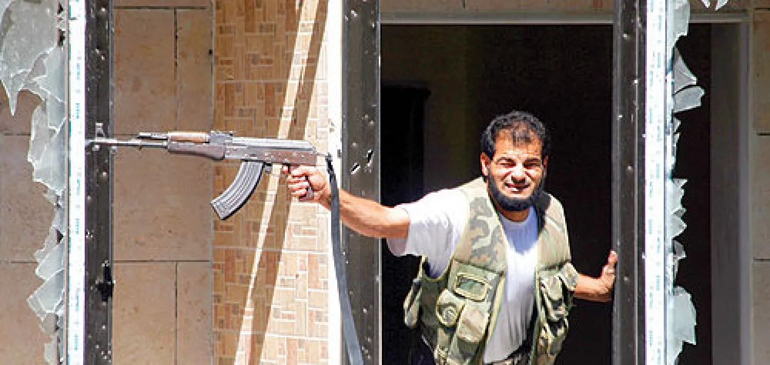 عنصر من الجيش السوري الحر يطلق النار من سلاحه نحو مبنى تحتله القوات النظامية التابعة لبشار الأسد(رويترز)