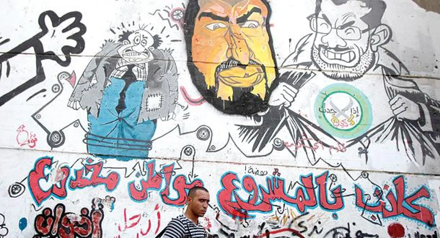 مصري يمر بجانب صور جدارية كاريكاتيرية للرئيس السابق محمد مرسي ونائب المرشد العام لجماعة الإخوان خيرت الشاطر في القاهرة (رويترز)