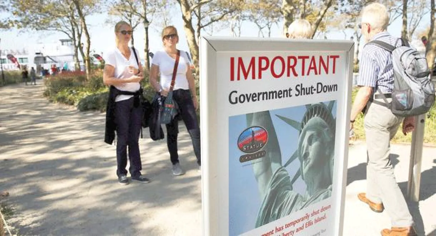أميركيتان تطالعان إعلانا عن إغلاق مقر تمثال الحرية في نيويورك بسبب الإقفال الجزئي لدوائر الحكومة الفيدرالية أمس (أ.ف.ب)