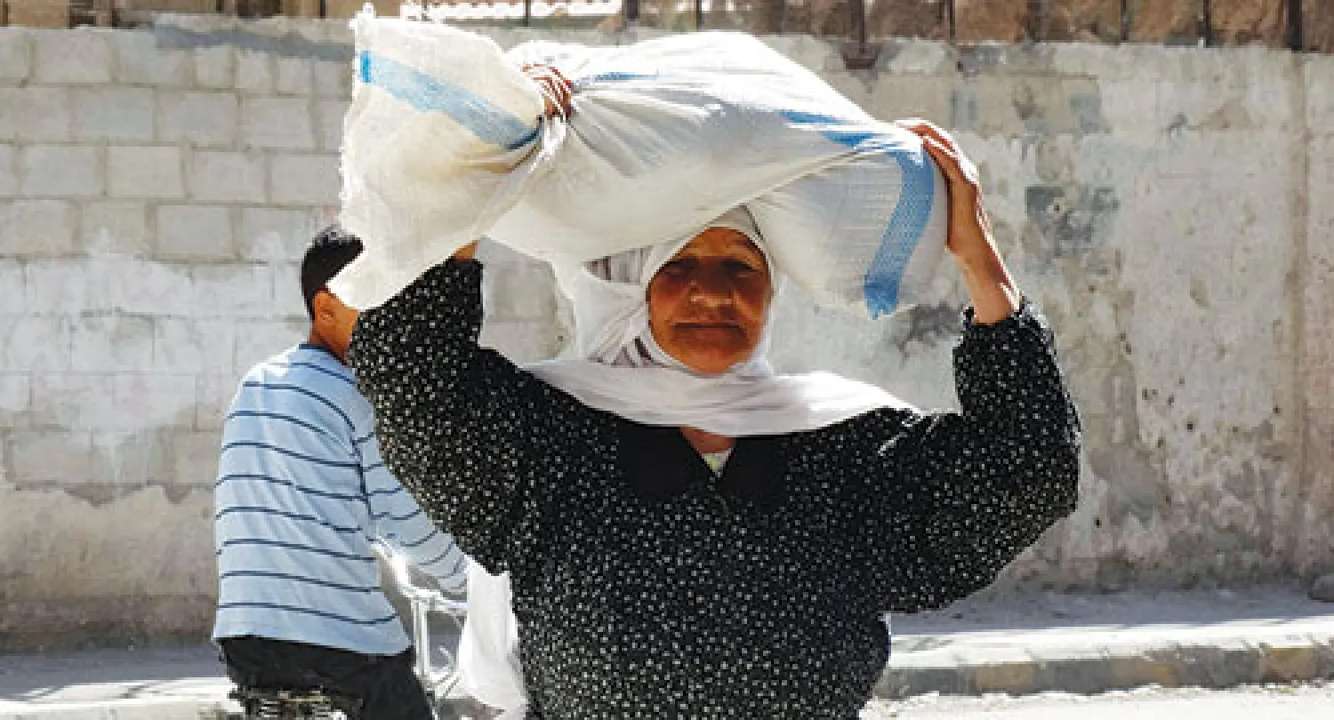 سورية تحمل كيس مساعدات غذائية في الغوطة بريف دمشق. وتحذر منظمات دولية من مجاعة في المنطقة جراء حصارها من قوات النظام (رويترز)