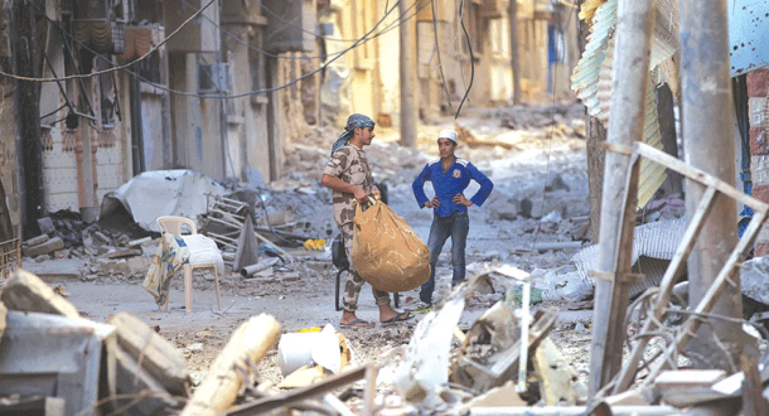 مقاتل سوري يحاول مساعدة مواطنين على حمل أمتعتهم من أنقاض أحد المباني المدمرة في إدلب أمس (رويترز)