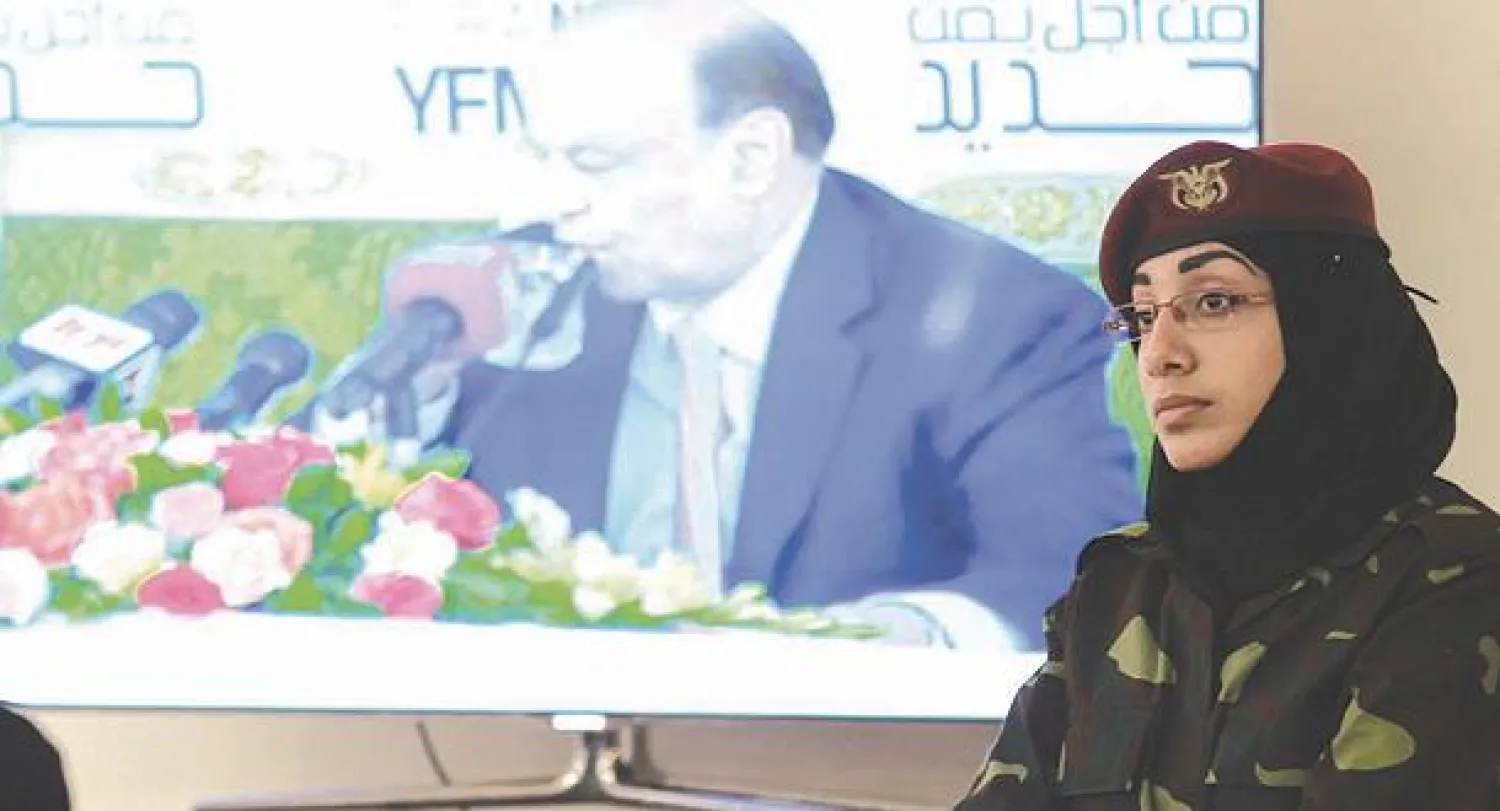 شرطية يمنية تقف بجانب شاشة كبيرة أثناء الكلمة الختامية للرئيس عبد ربه منصور هادي  لجلسات الحوار الوطني أمس (أ.ف.ب)