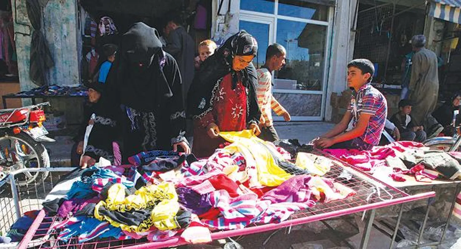 سوريات يقلبن ملابس في سوق منطقة المنبج بحلب قبيل عيد الأضحى (رويترز)