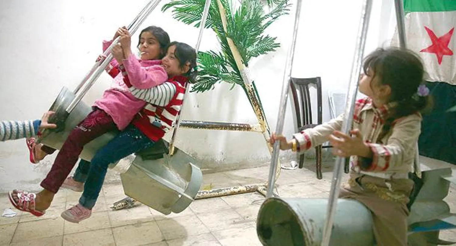 أطفال سوريون على مراجيح صنعت من مخلفات صواريخ روسية في احتفالات العيد بدوما في ريف دمشق (رويترز)